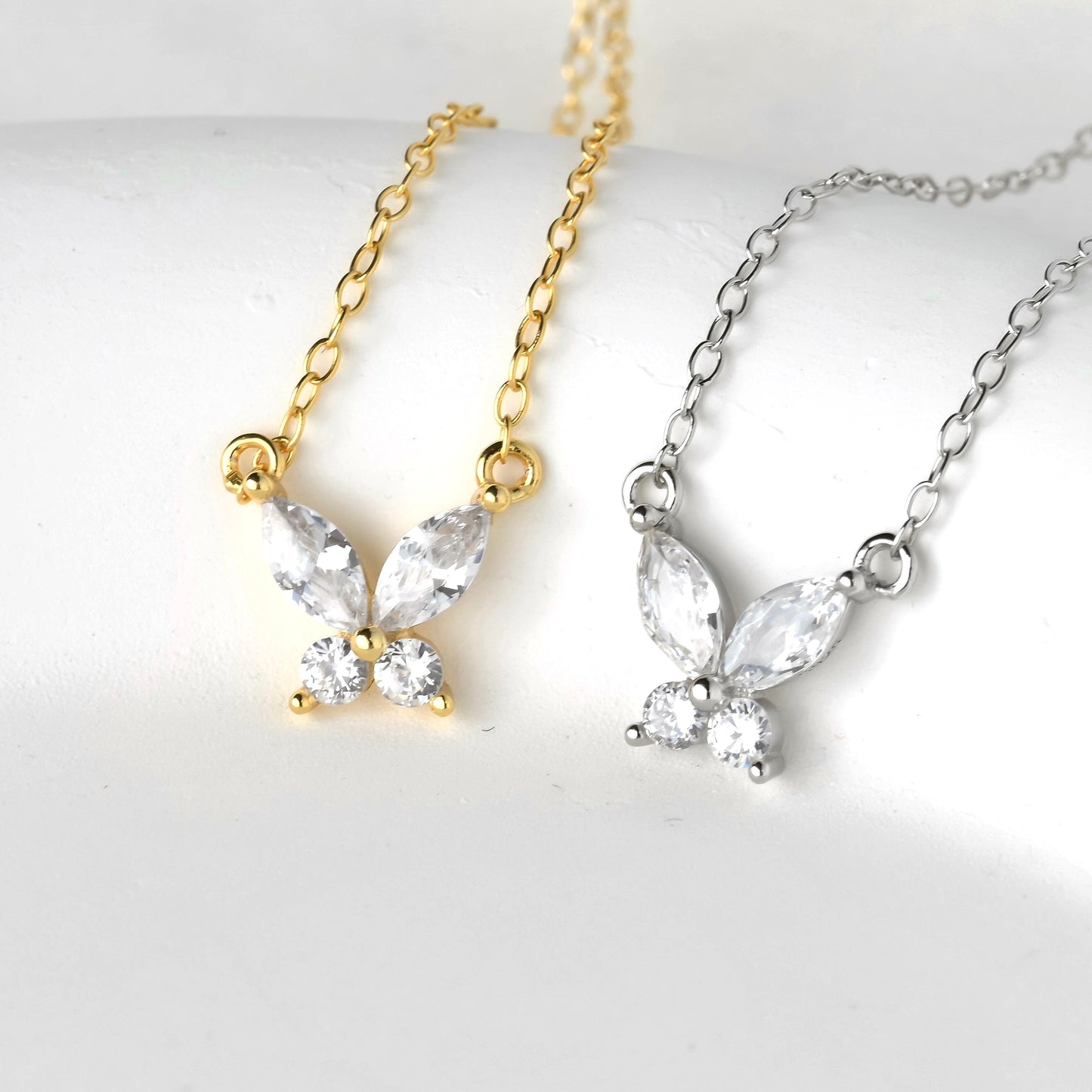Two necklaces, one gold and one silver, with marquise butterfly pendants on a white background