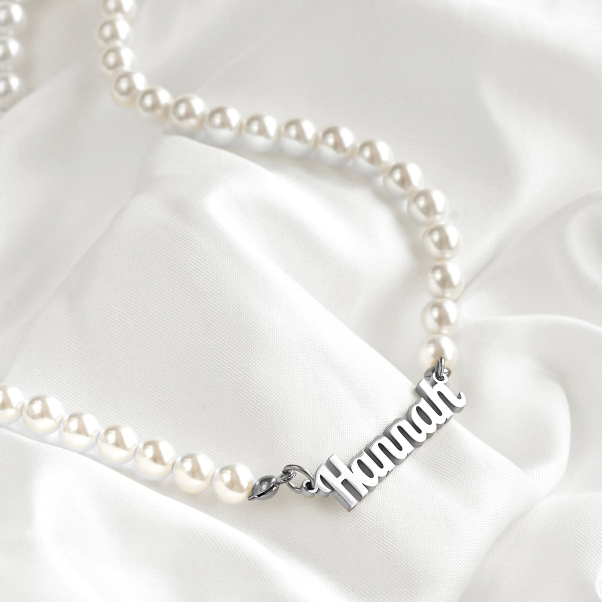 Round shell pearl necklace with the name "Hannah" in silver stainless steel draped on white satin.
