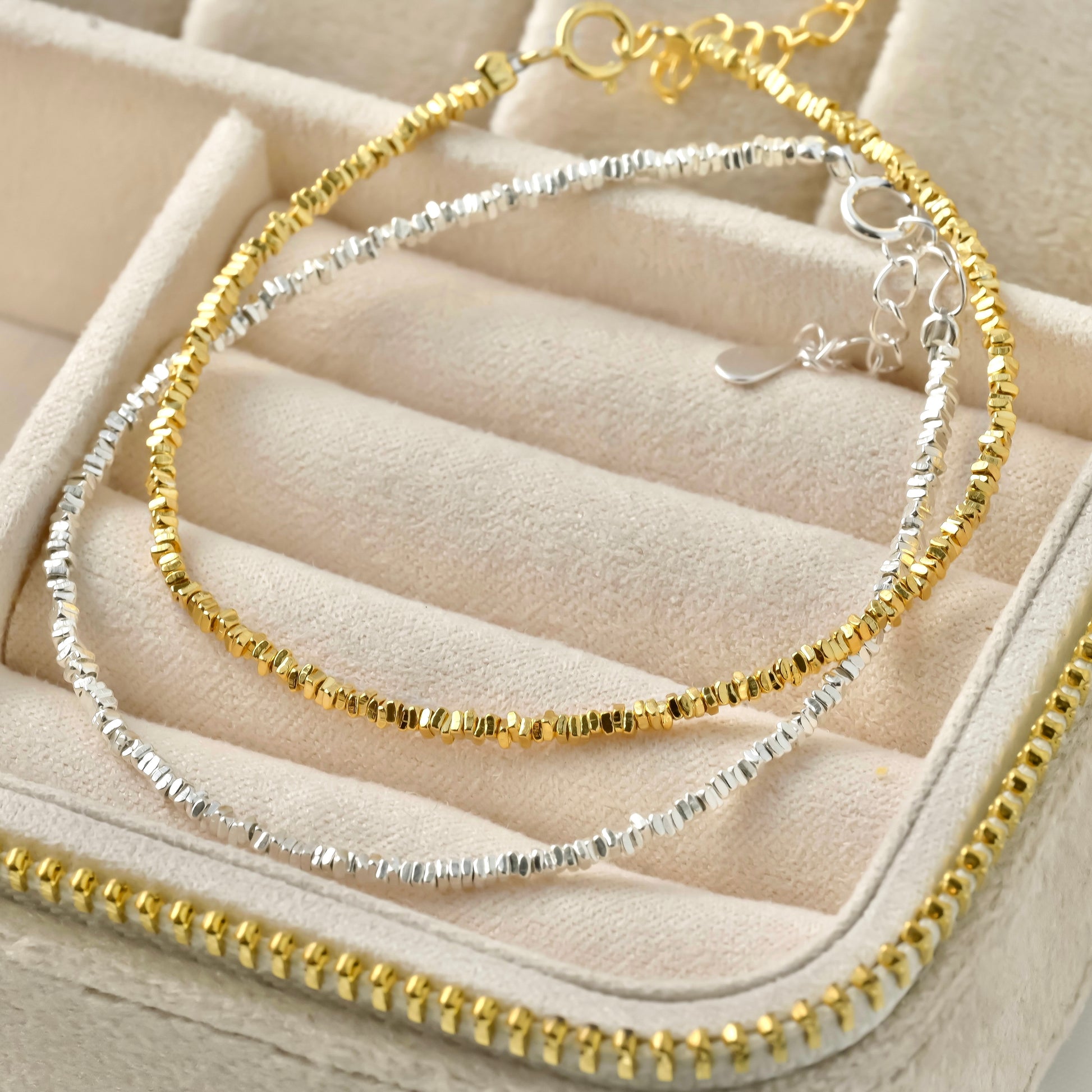 Two gold and silver beaded bracelets on a beige jewelry display.