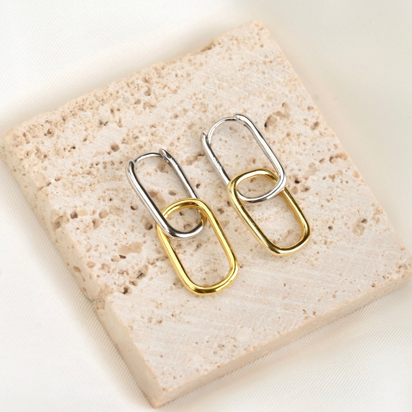 Pair of rectangular two tone earrings with top link silver and bottom link gold on a textured stone surface