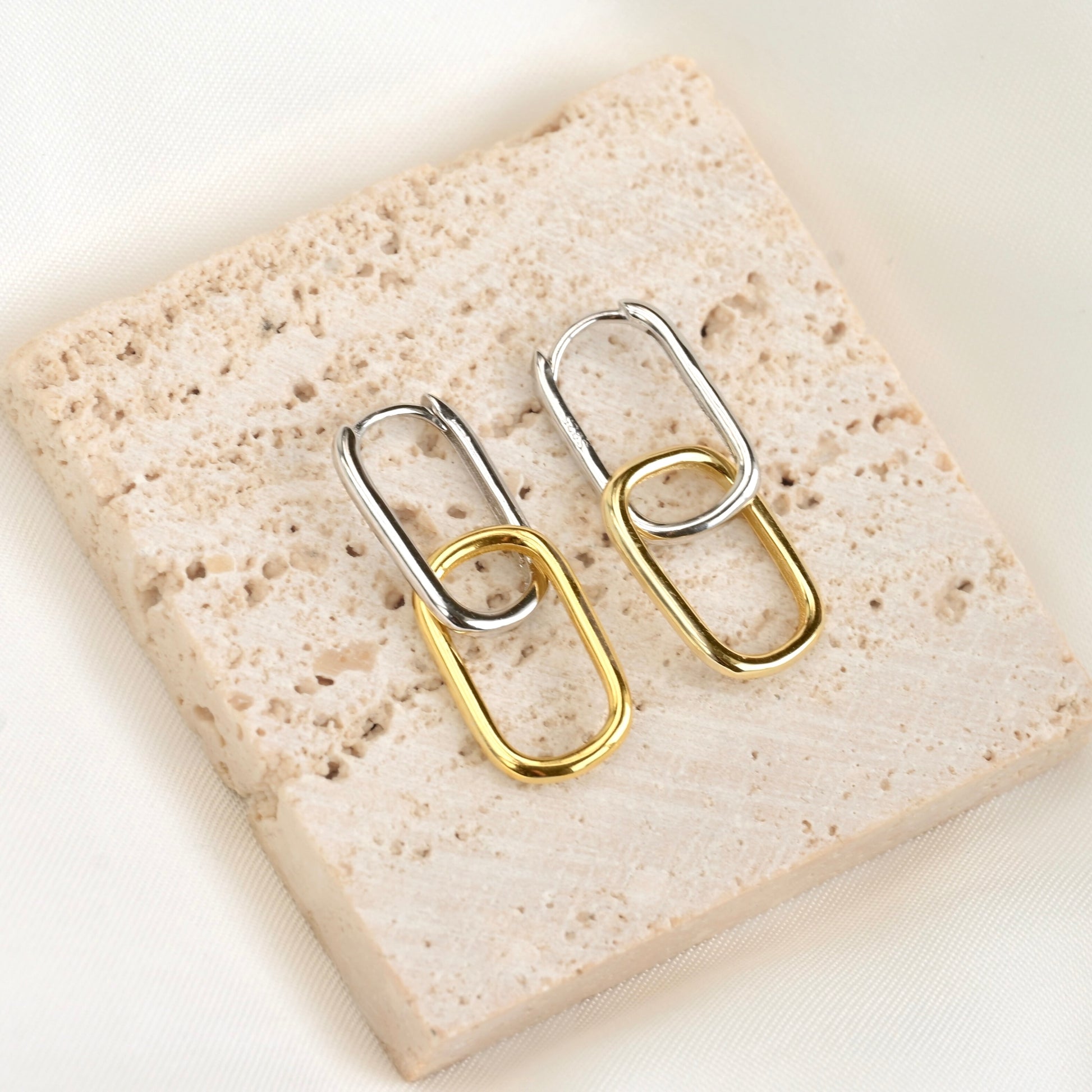 Pair of rectangular two tone earrings with top link silver and bottom link gold on a textured stone surface