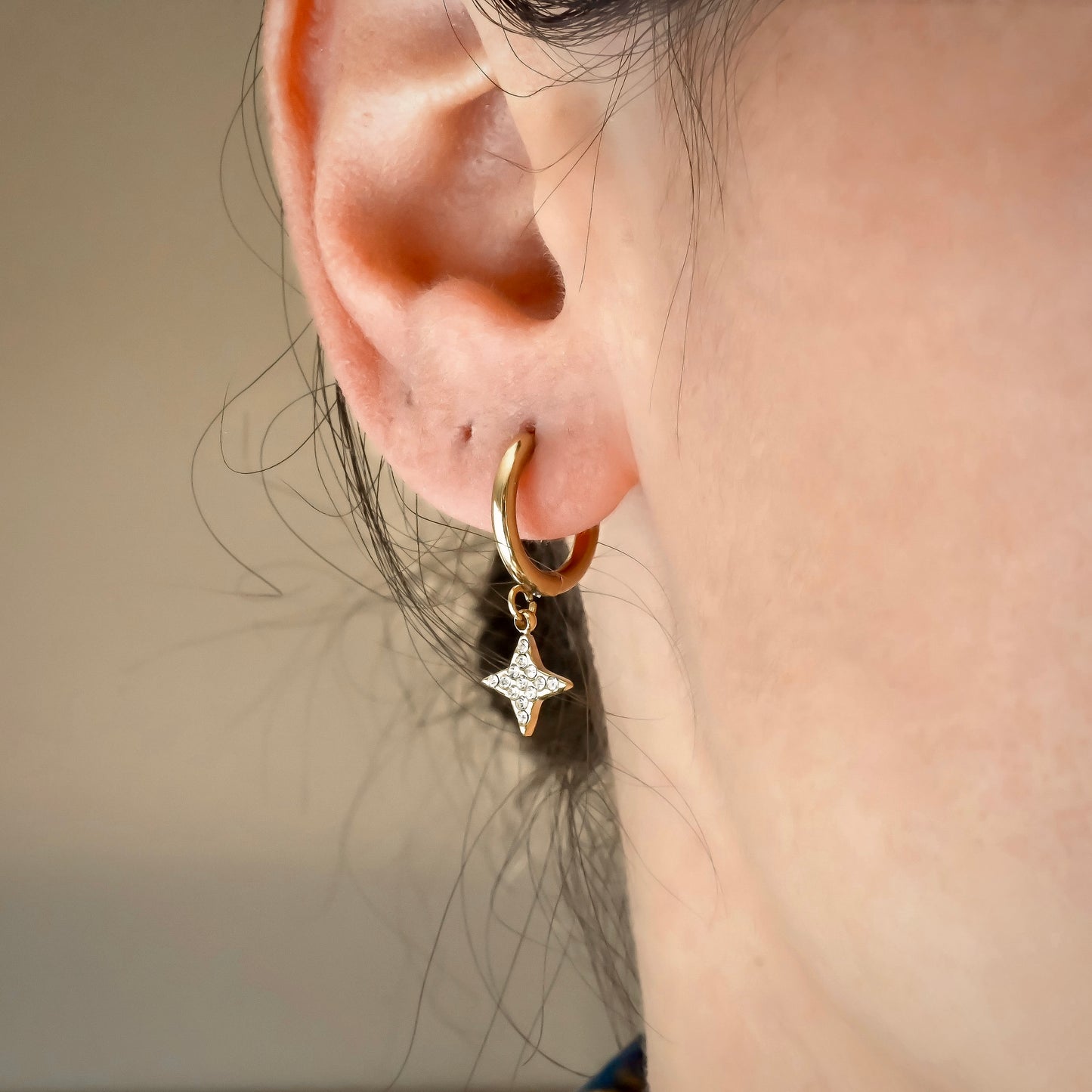 Close-up of an ear wearing a gold hoop earring with a spark-shaped charm resembling a star.
