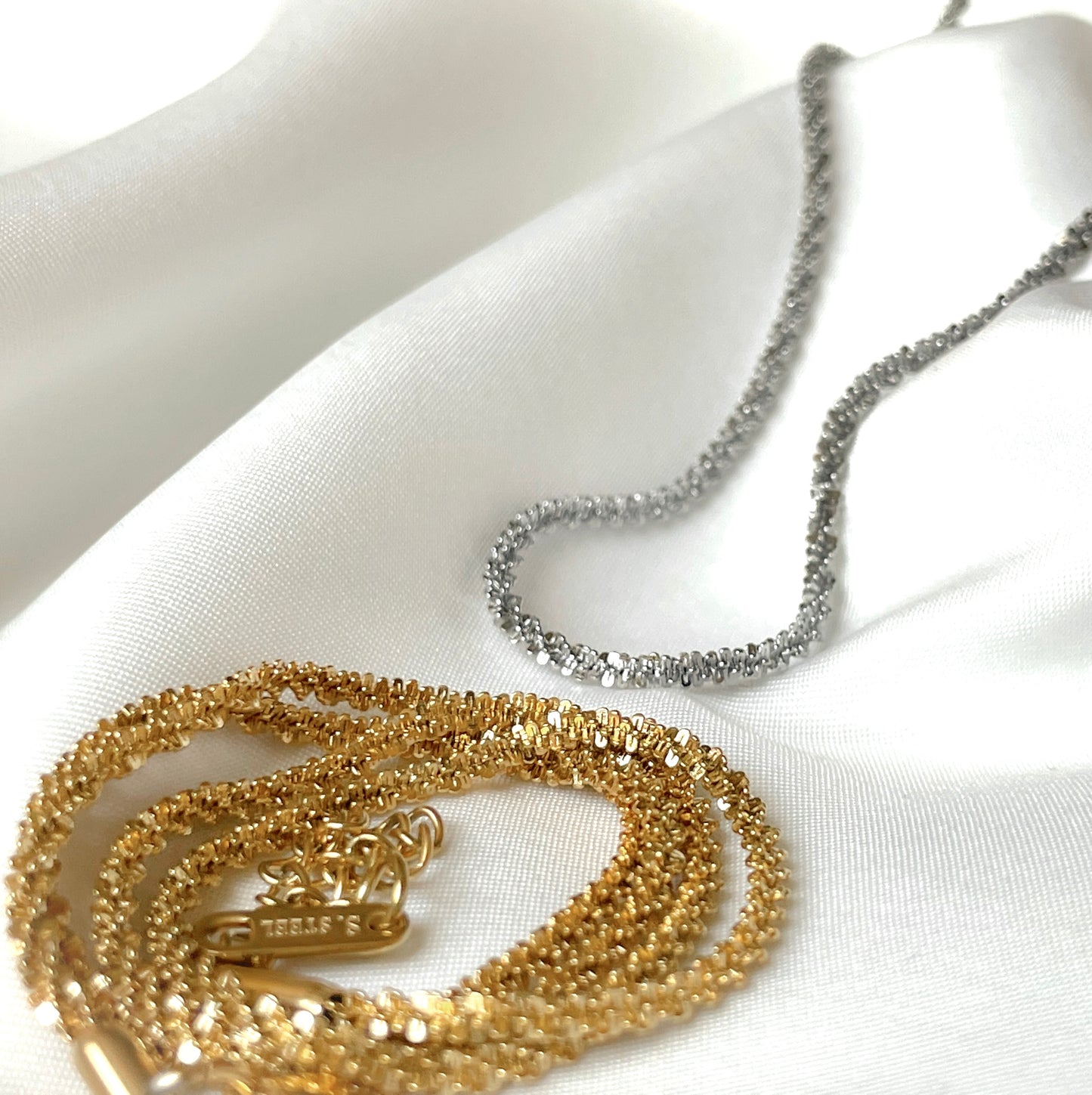 Gold and silver sparkle necklaces on a white fabric background