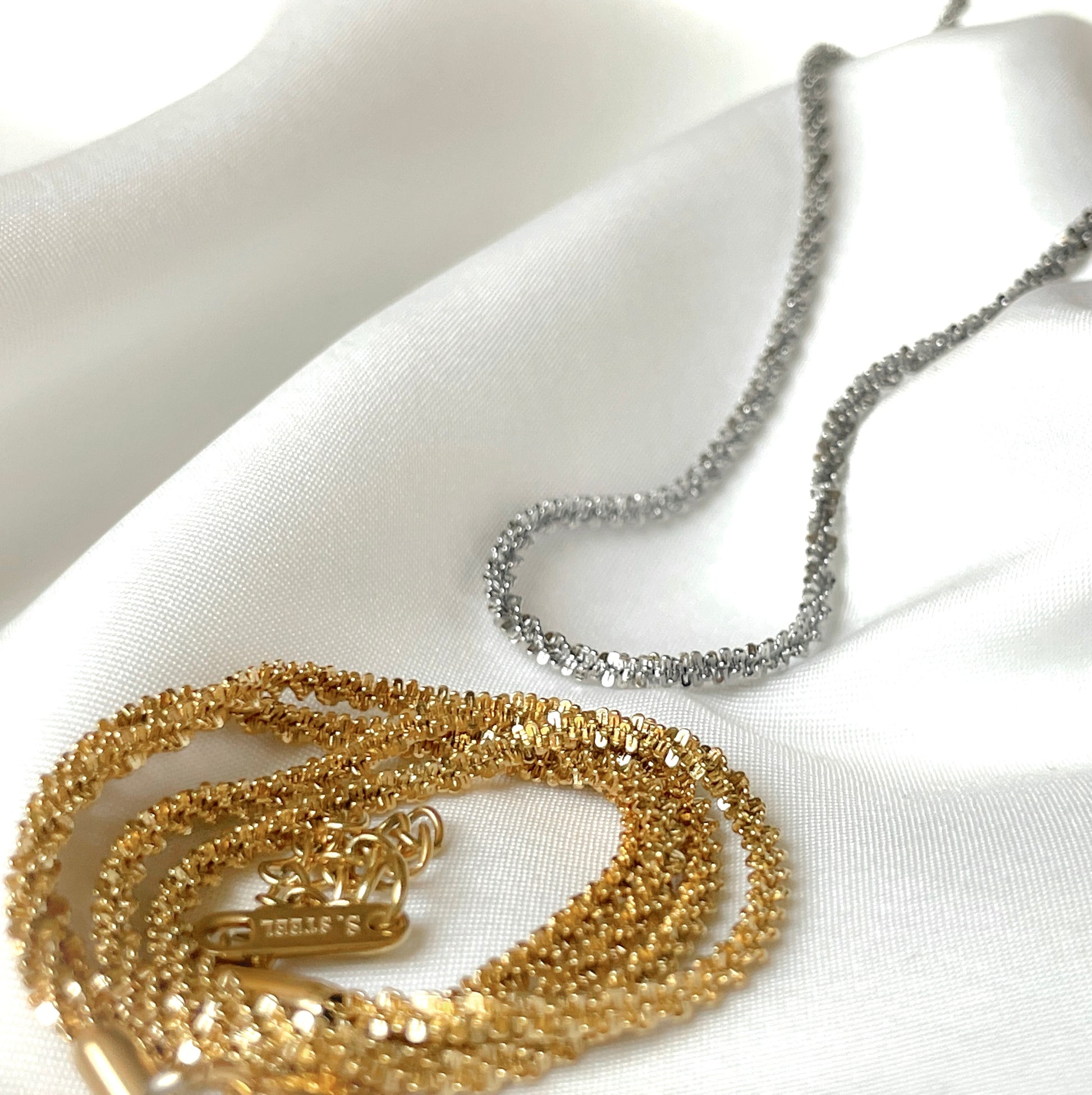 Gold and silver sparkle necklaces on a white fabric background