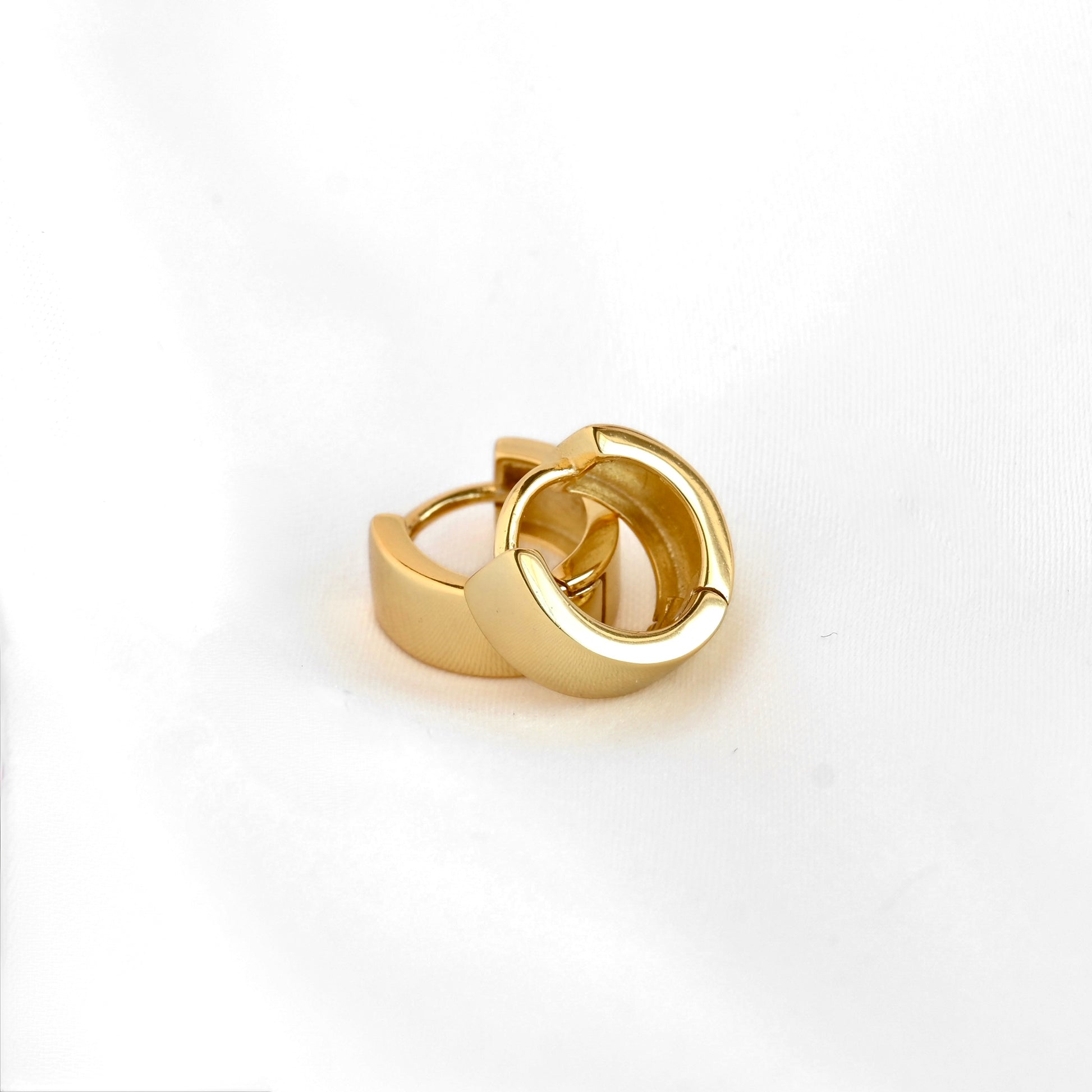 A pair of gold huggie hoop earrings with a polished finish, displayed on a clean white background.