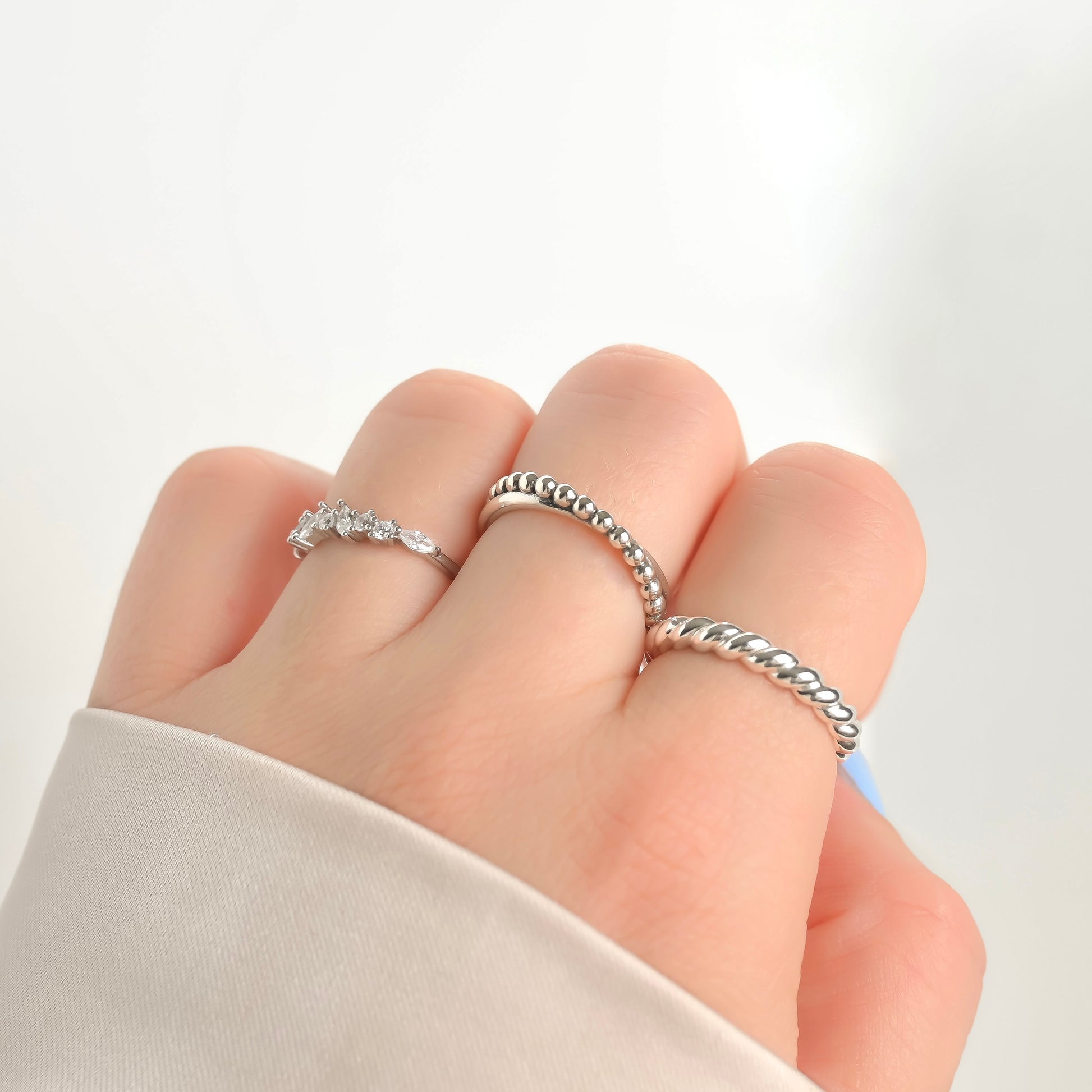 Close-up of a hand with fist pose, wearing three silver rings on a light background