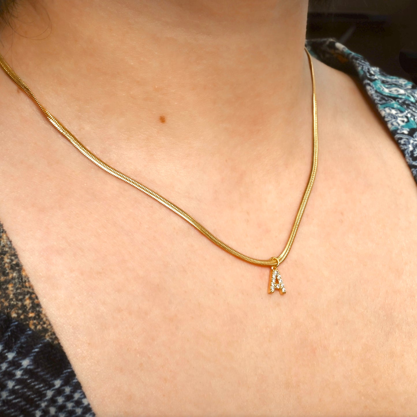 Gold initial necklace with a snake chain on a person's neck