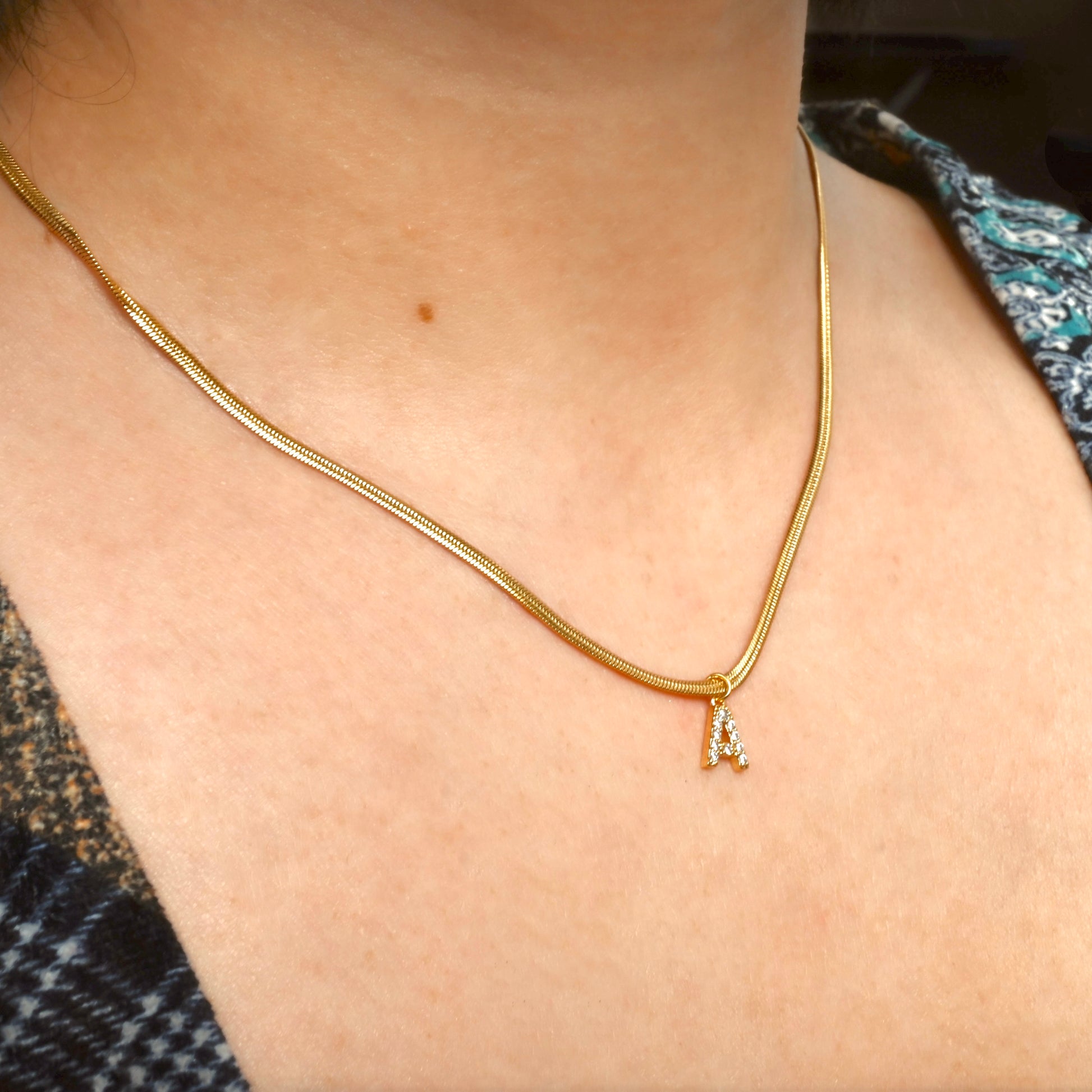 Gold initial necklace with a snake chain on a person's neck