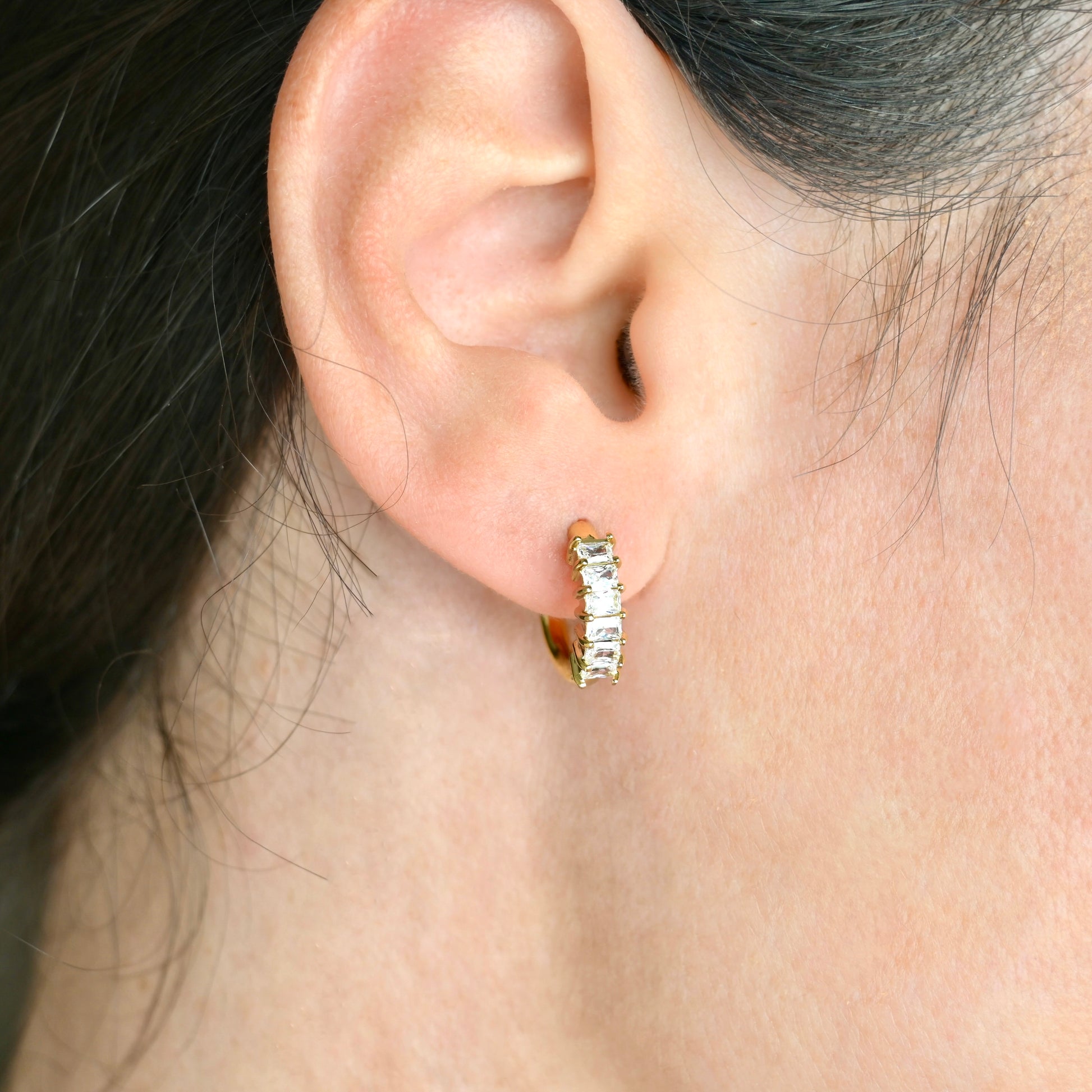 Gold hoop earrings worn by a person with dark hair.
