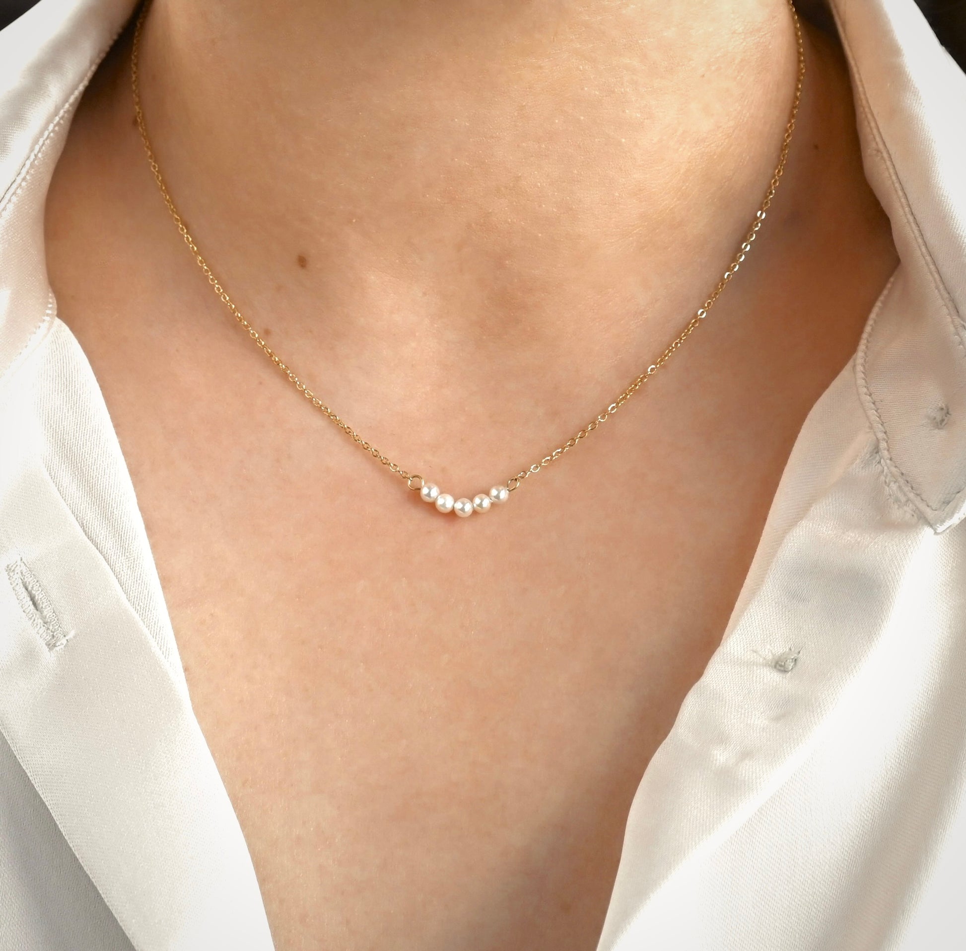 Gold necklace with pearls worn by a person in a white shirt