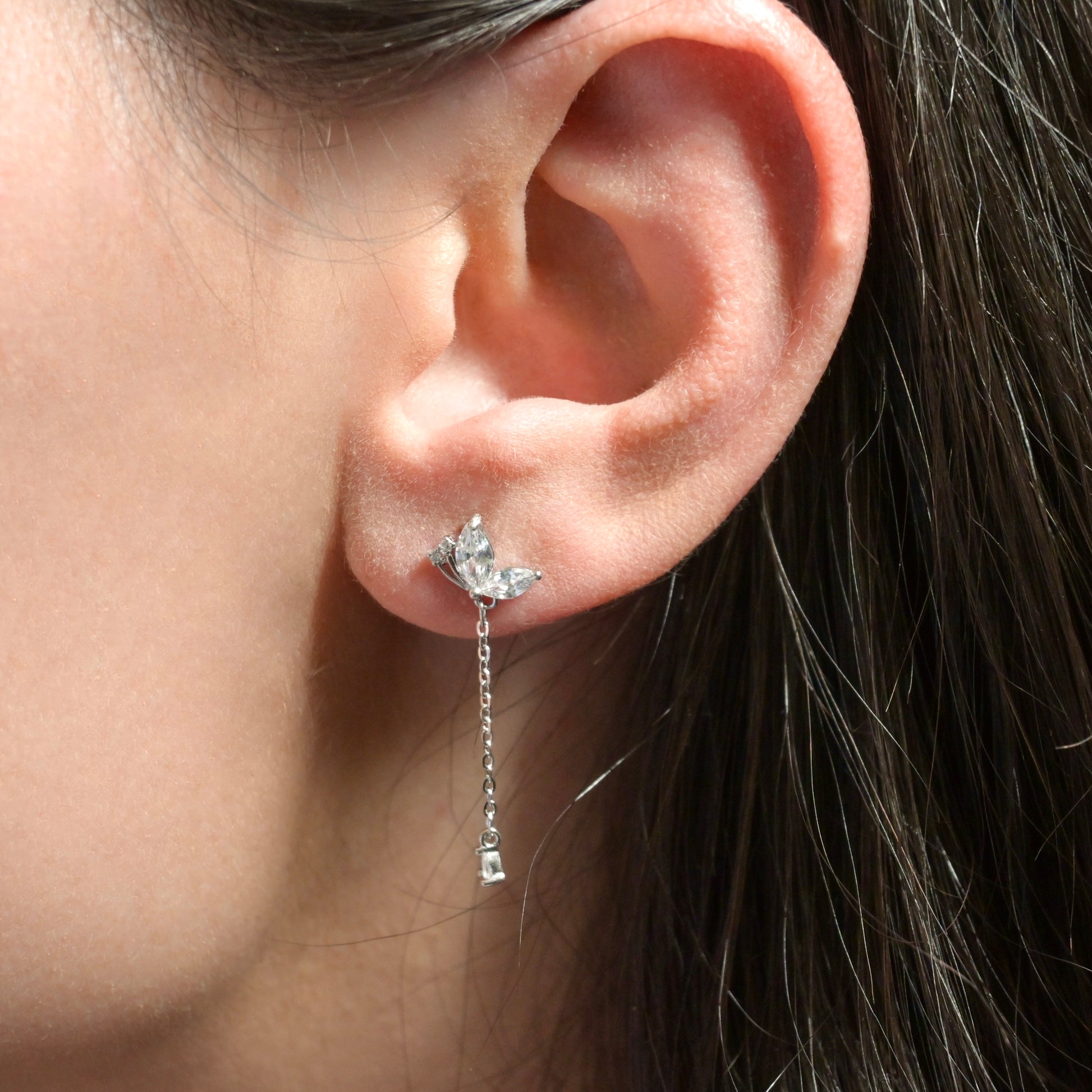 Close-up of an ear wearing a silver diamond earring with a chain drop