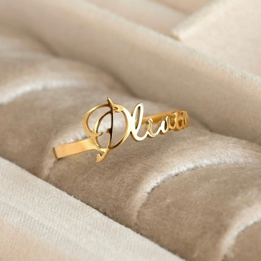 Personalized Gold name ring with 'Olivia' script on a beige textured surface