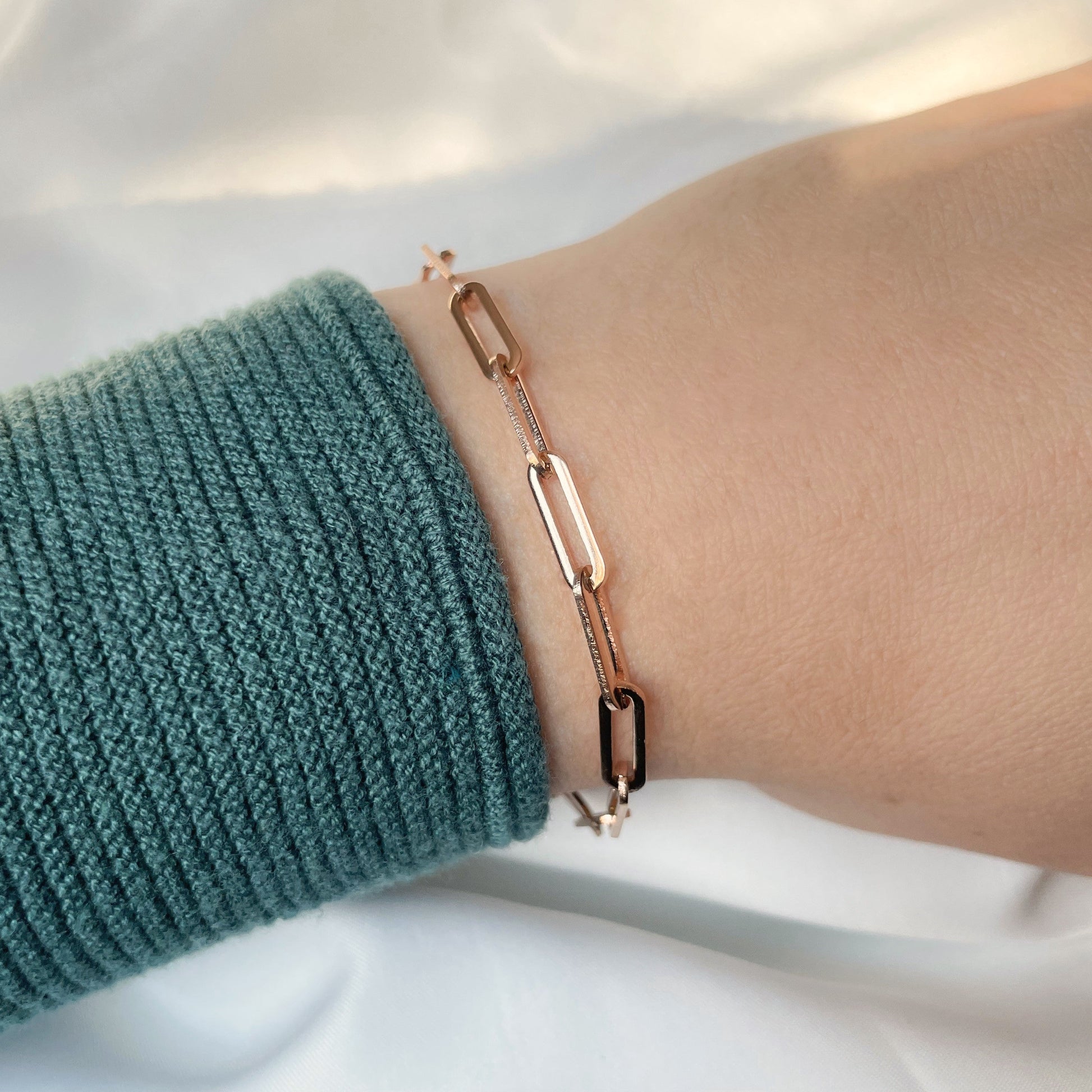 Bold Rose gold paperclip chain bracelet on a wrist with a green sleeve against a white background
