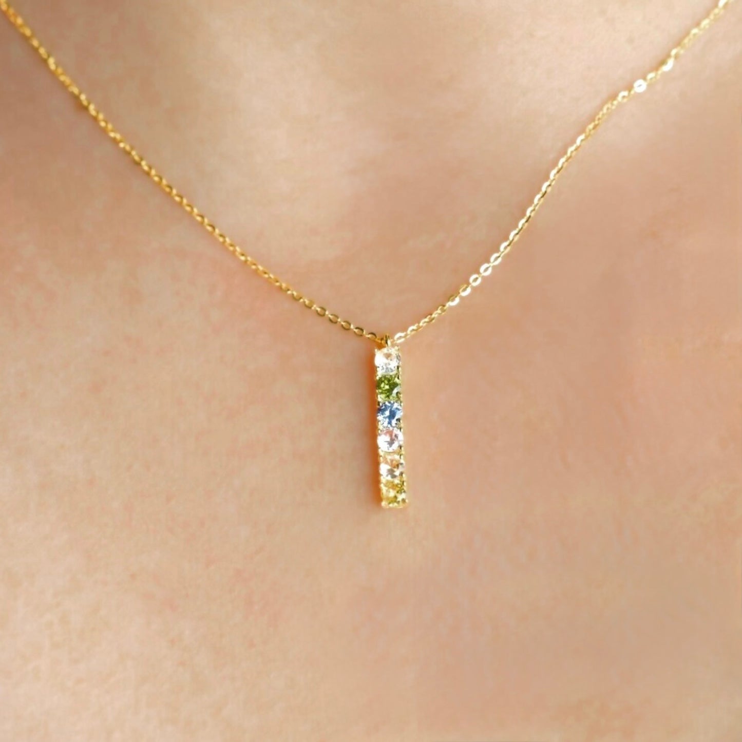 Gold necklace with a small pendant featuring colored stones on a person's neck.