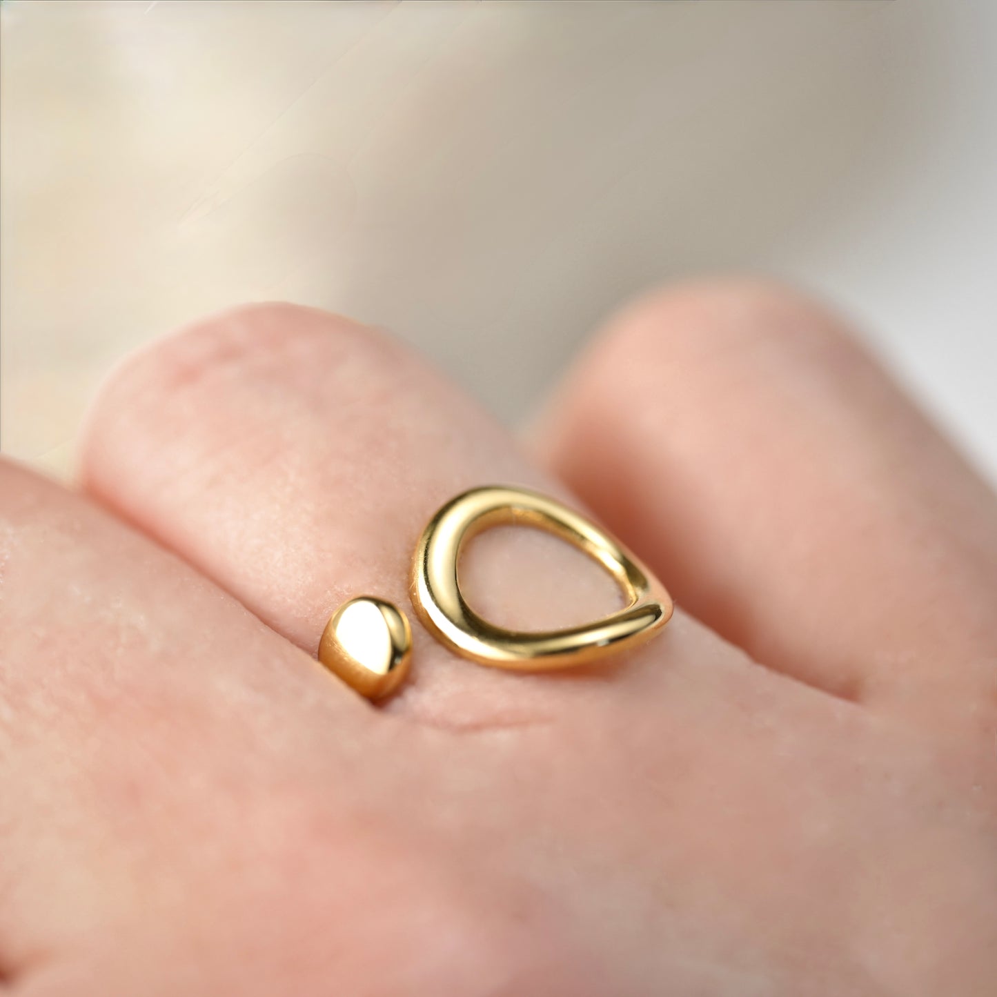 adjustable gold  ring on a finger against a neutral background