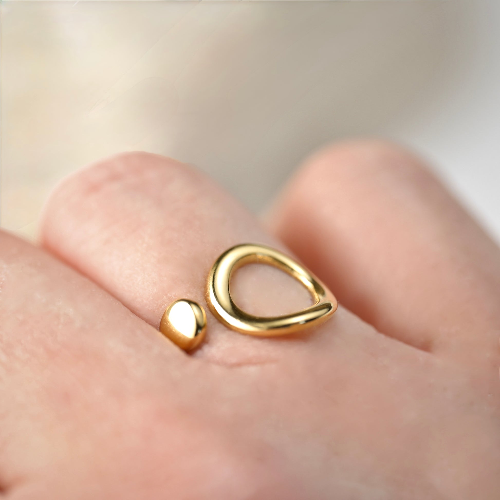 adjustable gold  ring on a finger against a neutral background