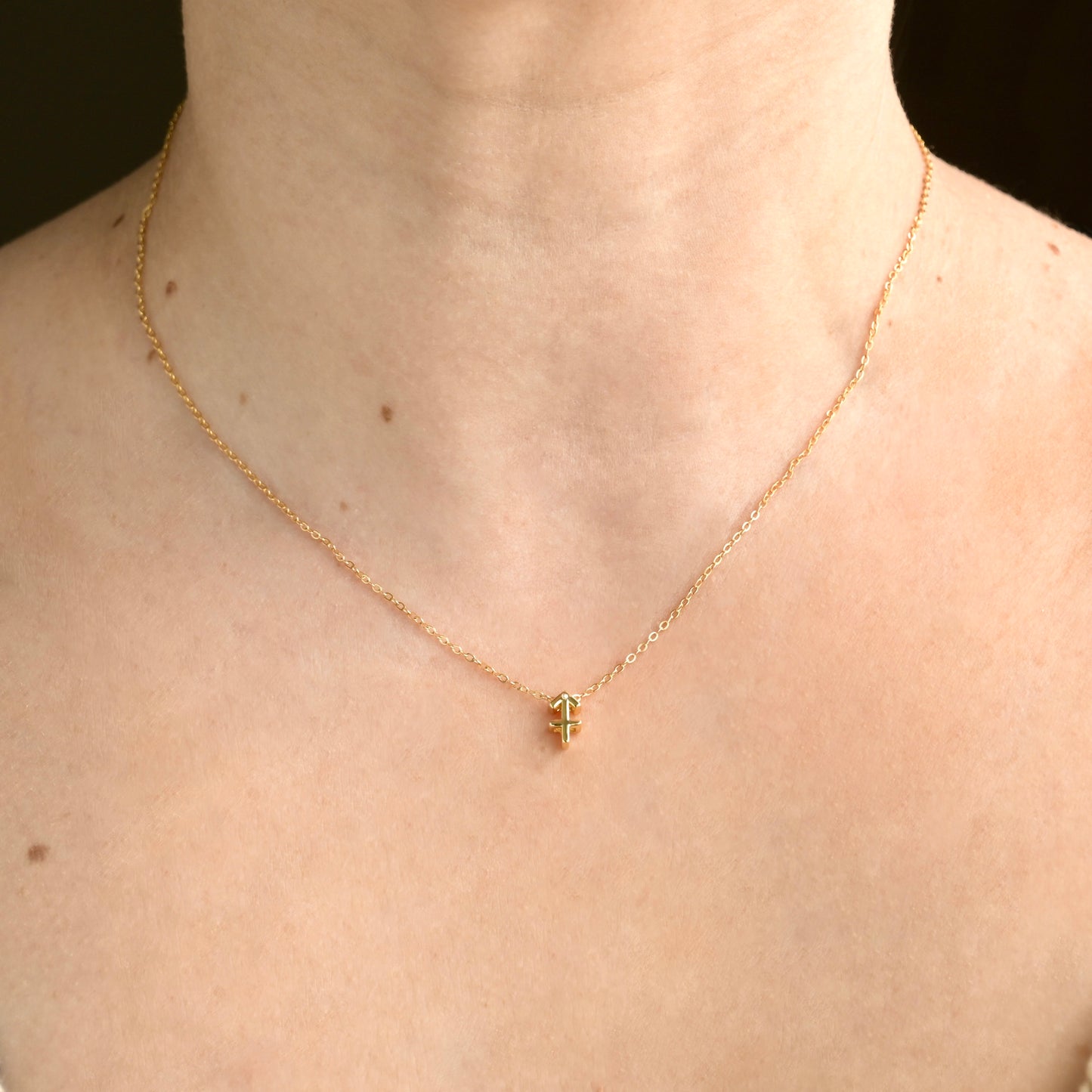 Gold sagittarius pendant necklace on a person's neck against a dark background