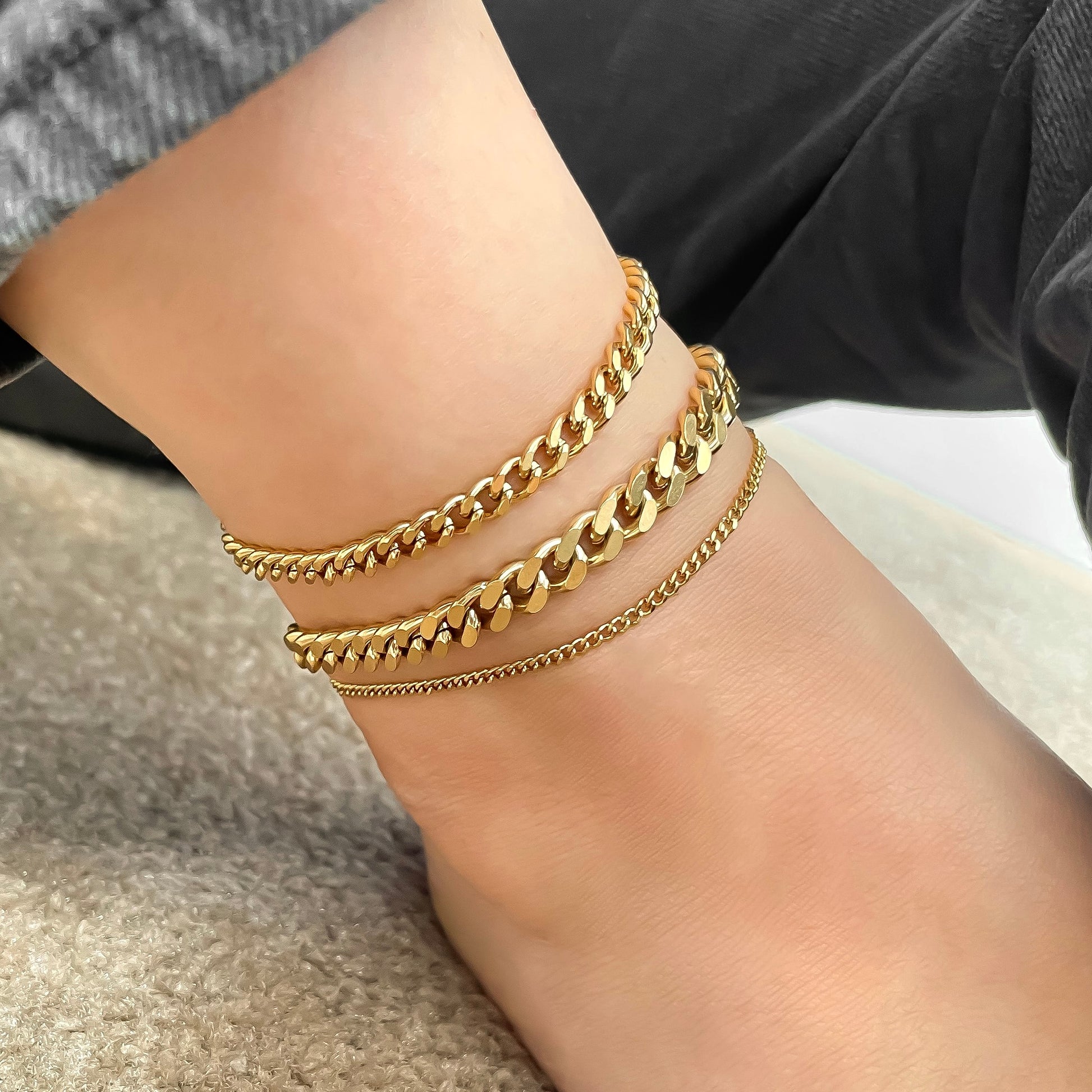 Gold curb chain anklets on a person's ankle with a neutral background