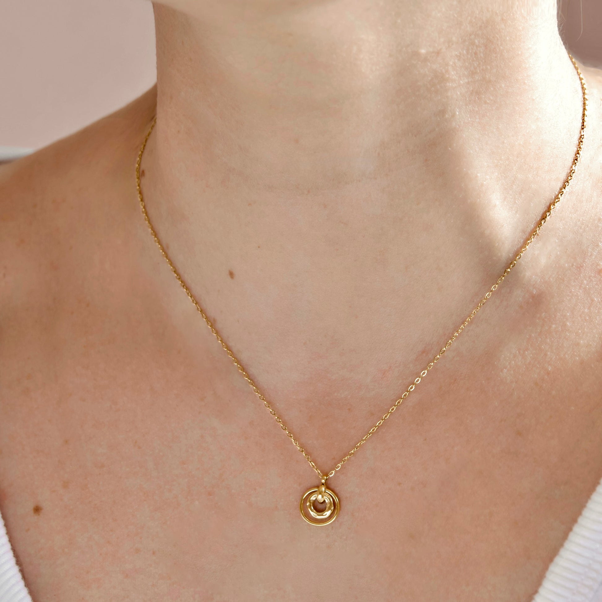 A close-up of a person's neck and upper chest wearing a delicate gold chain necklace with a small circular gold pendant.