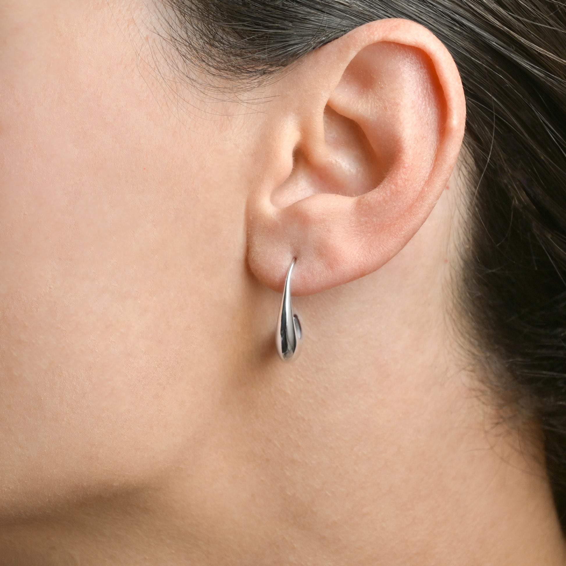 Close-up of an ear wearing a silver earring with a blurred background