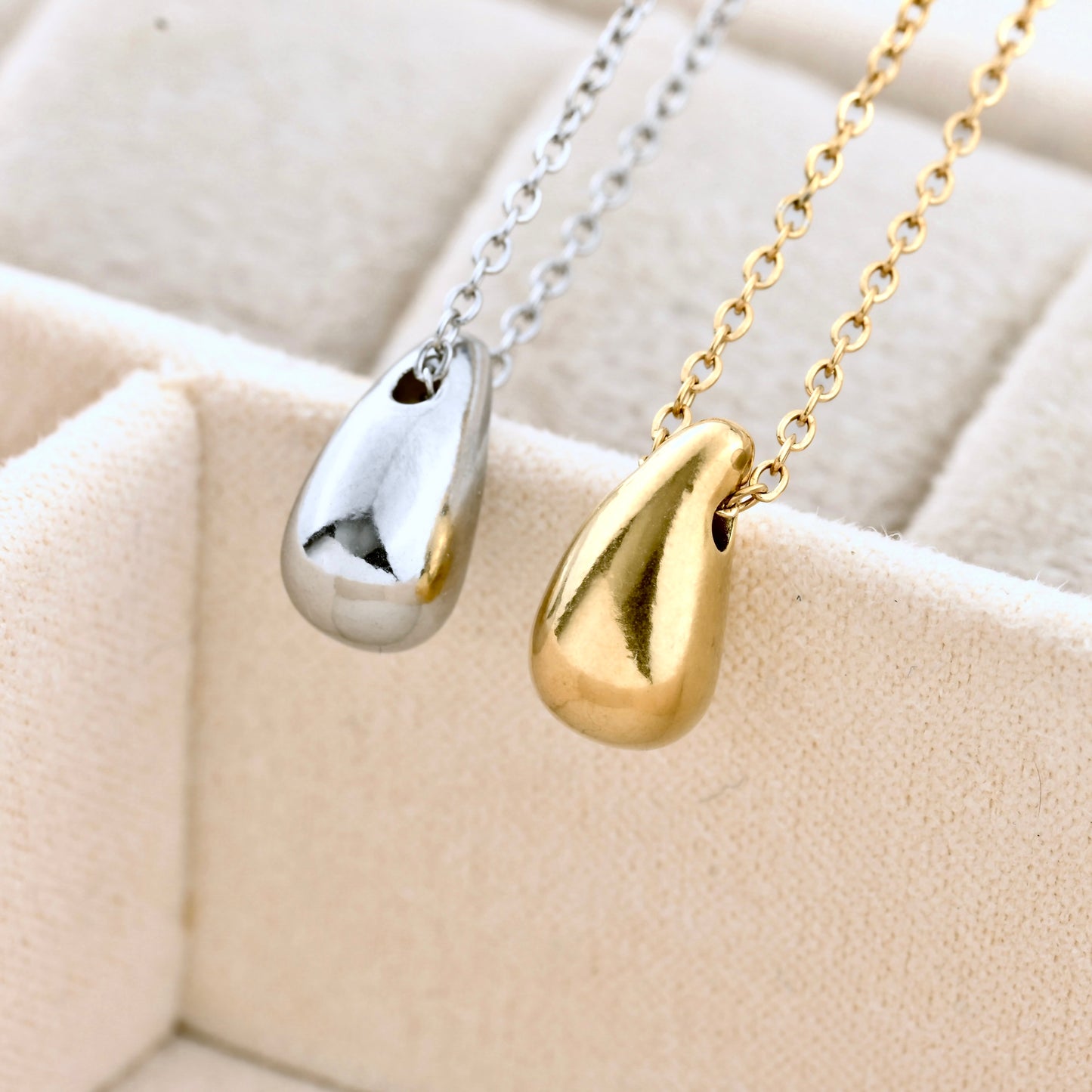 Gold and silver droplet pendants on cable chains against a beige textured background