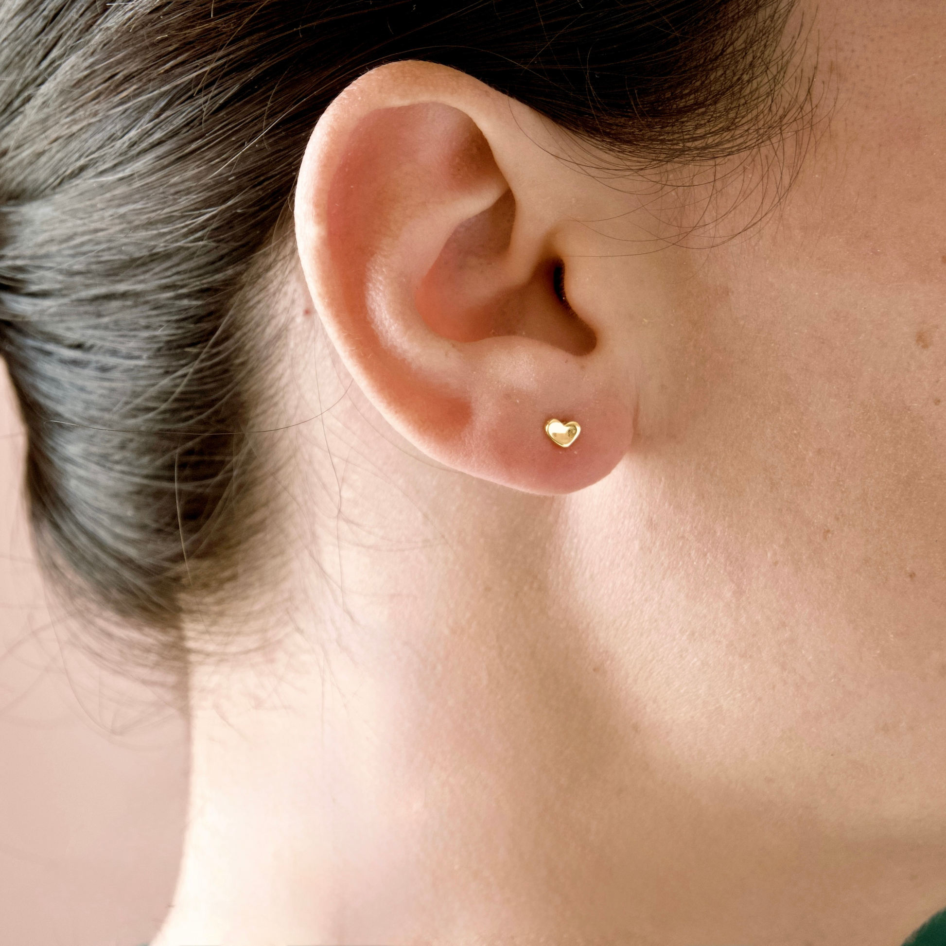 A close-up of a person's ear wearing a small gold heart stud earring.