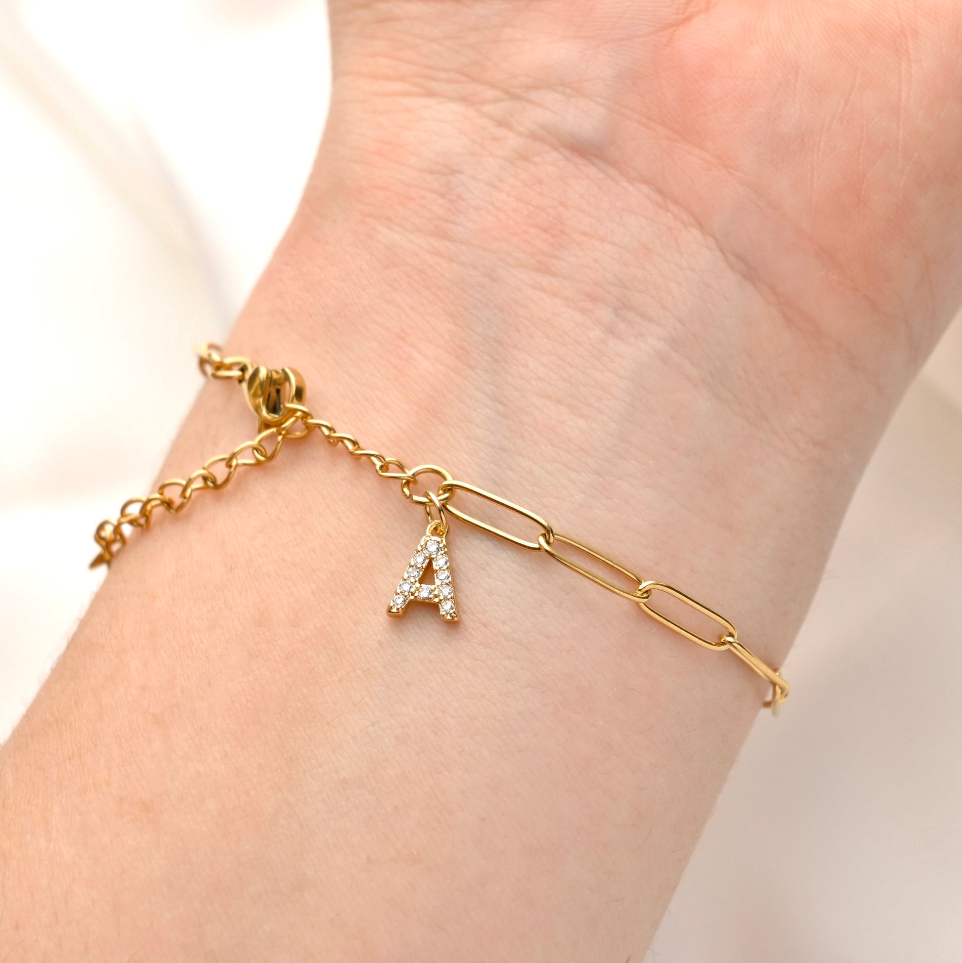 Gold chain bracelet with a CZ letter 'A' charm on a wrist against a neutral background