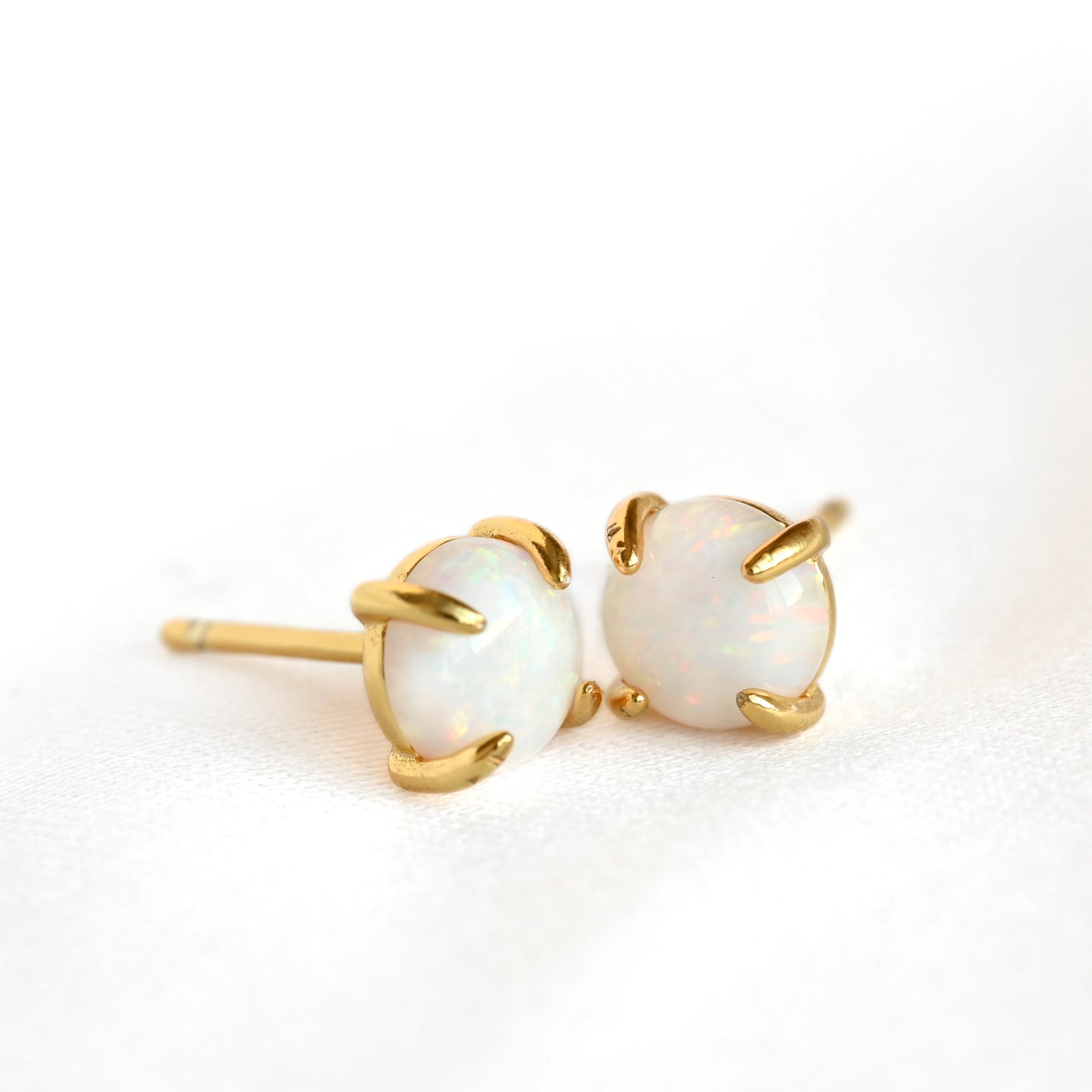A pair of gold stud earrings with oval white opal gemstones in a four-prong setting, photographed on a clean white background.