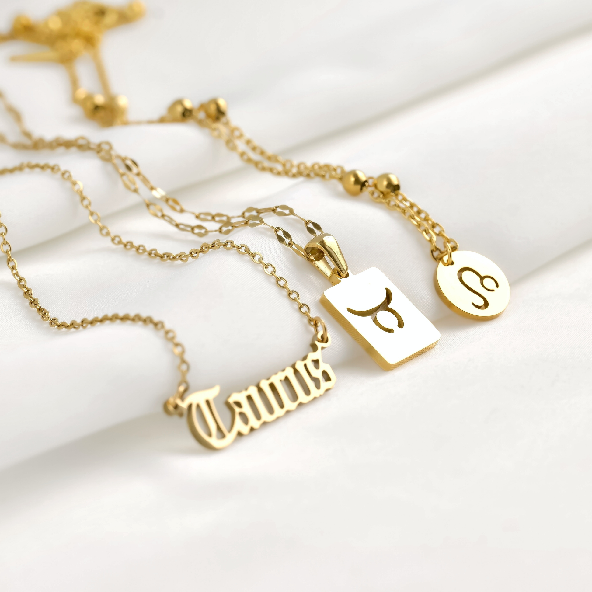 Gold necklaces with zodiac symbols on various chain designs on a white background