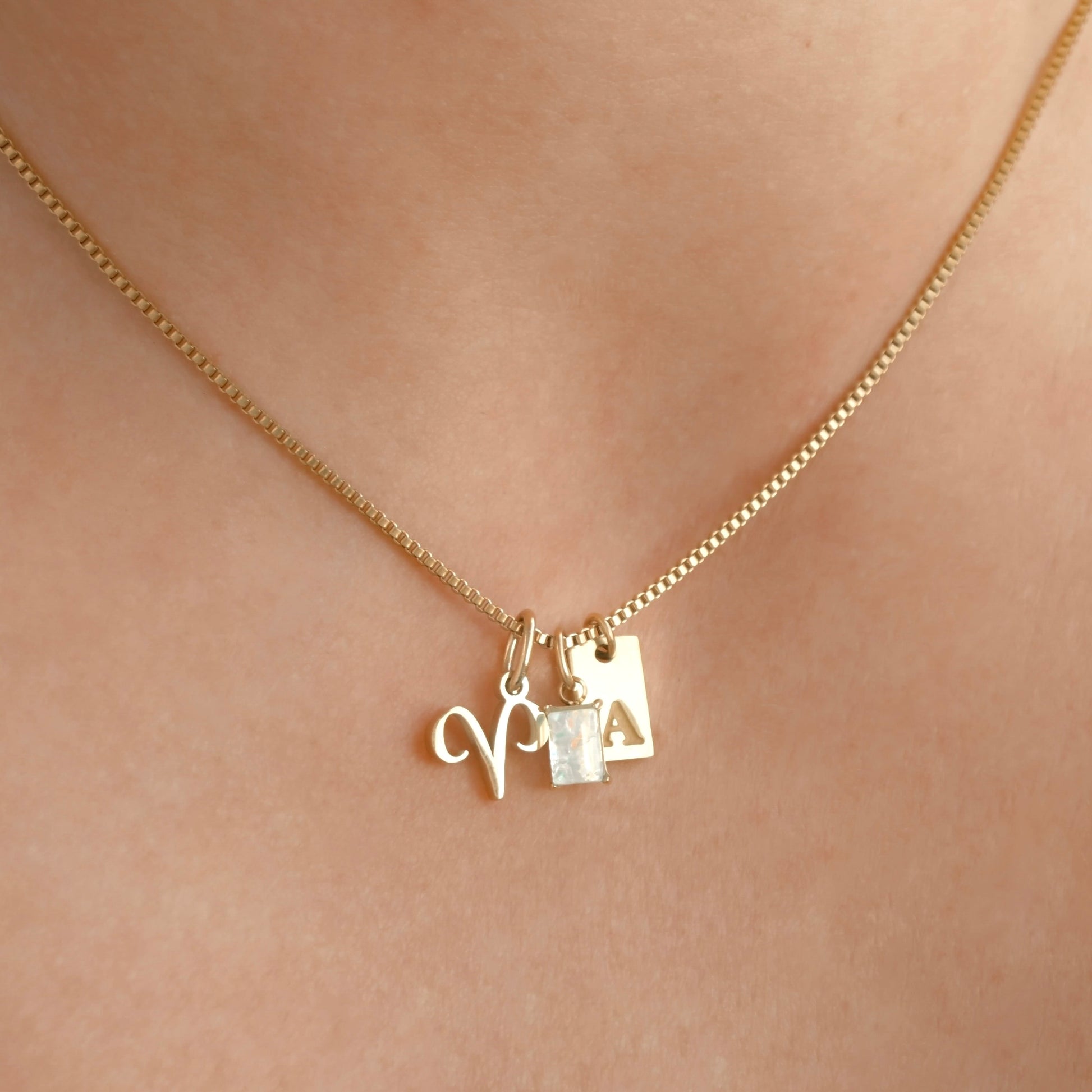 Gold box chain necklace with charms on a person's neck against a neutral background