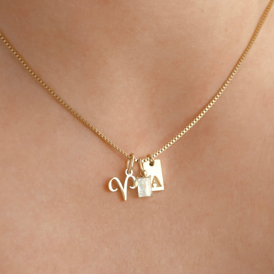 Gold box chain necklace with charms on a person's neck against a neutral background