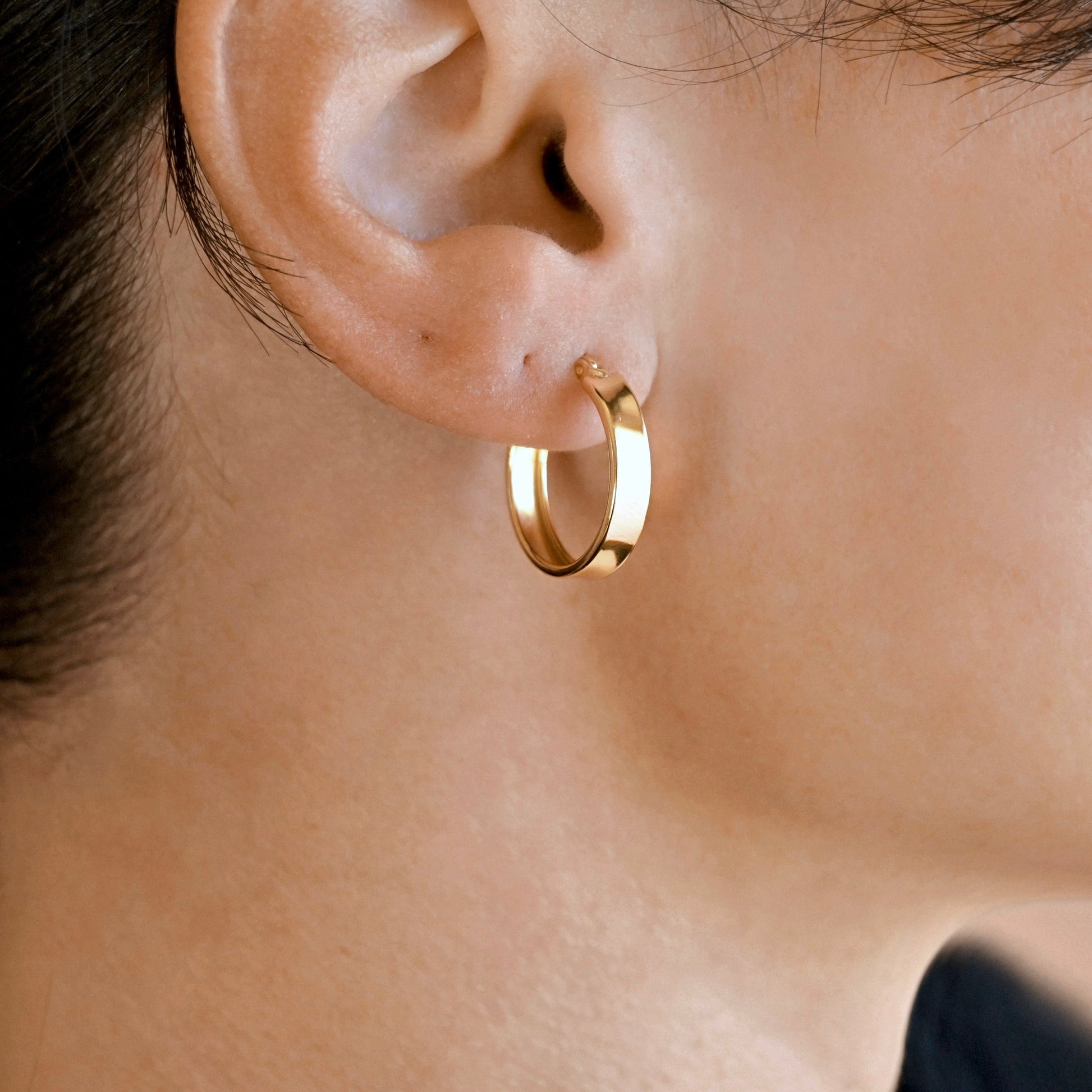 A close-up of a person's ear wearing a polished gold hoop earring.