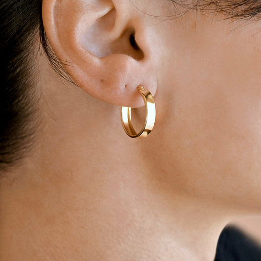 A close-up of a person's ear wearing a polished gold hoop earring.
