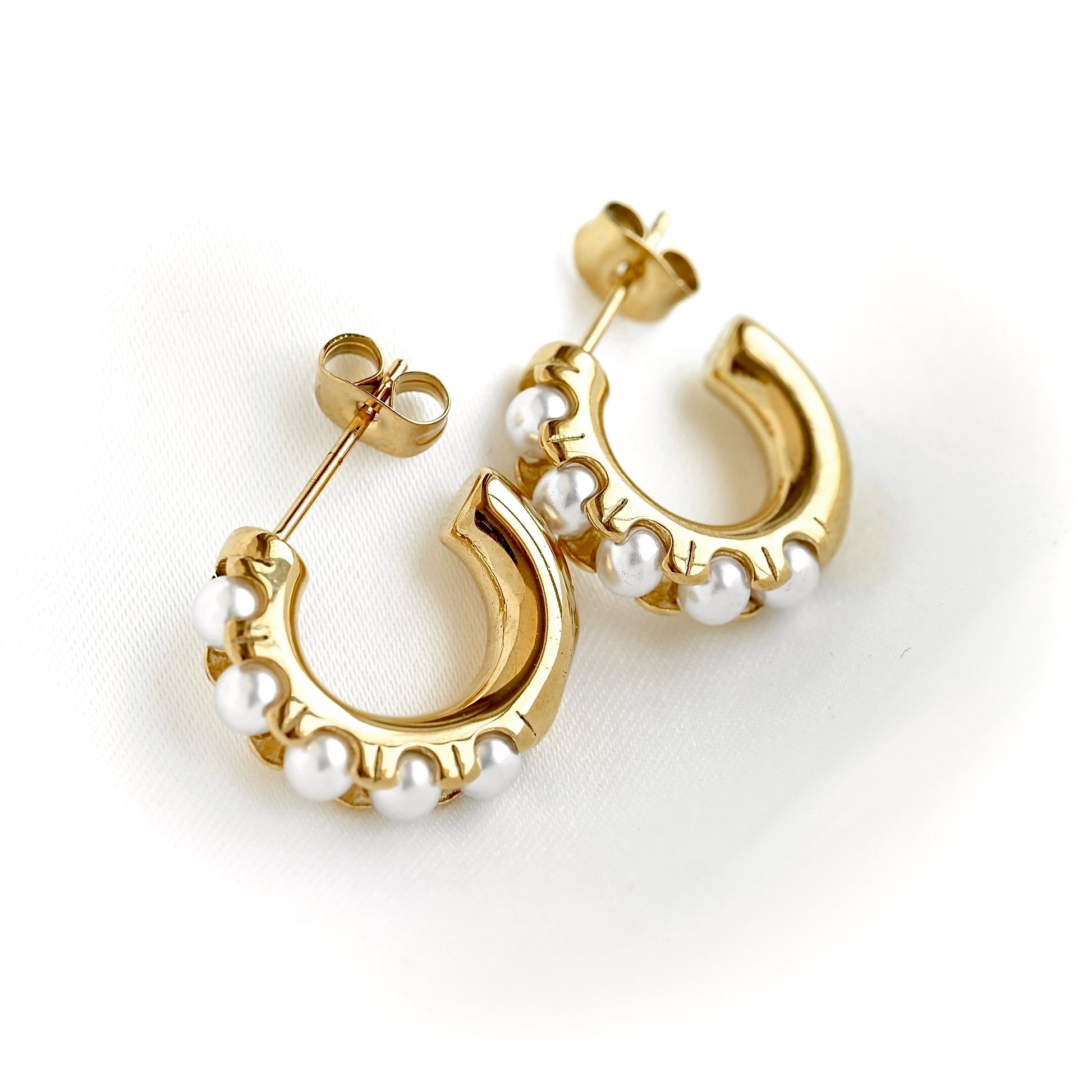 A pair of gold crescent-shaped hoop earrings decorated with small white pearls, shown on a clean white background.
