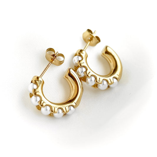 A pair of gold crescent-shaped hoop earrings decorated with small white pearls, shown on a clean white background.