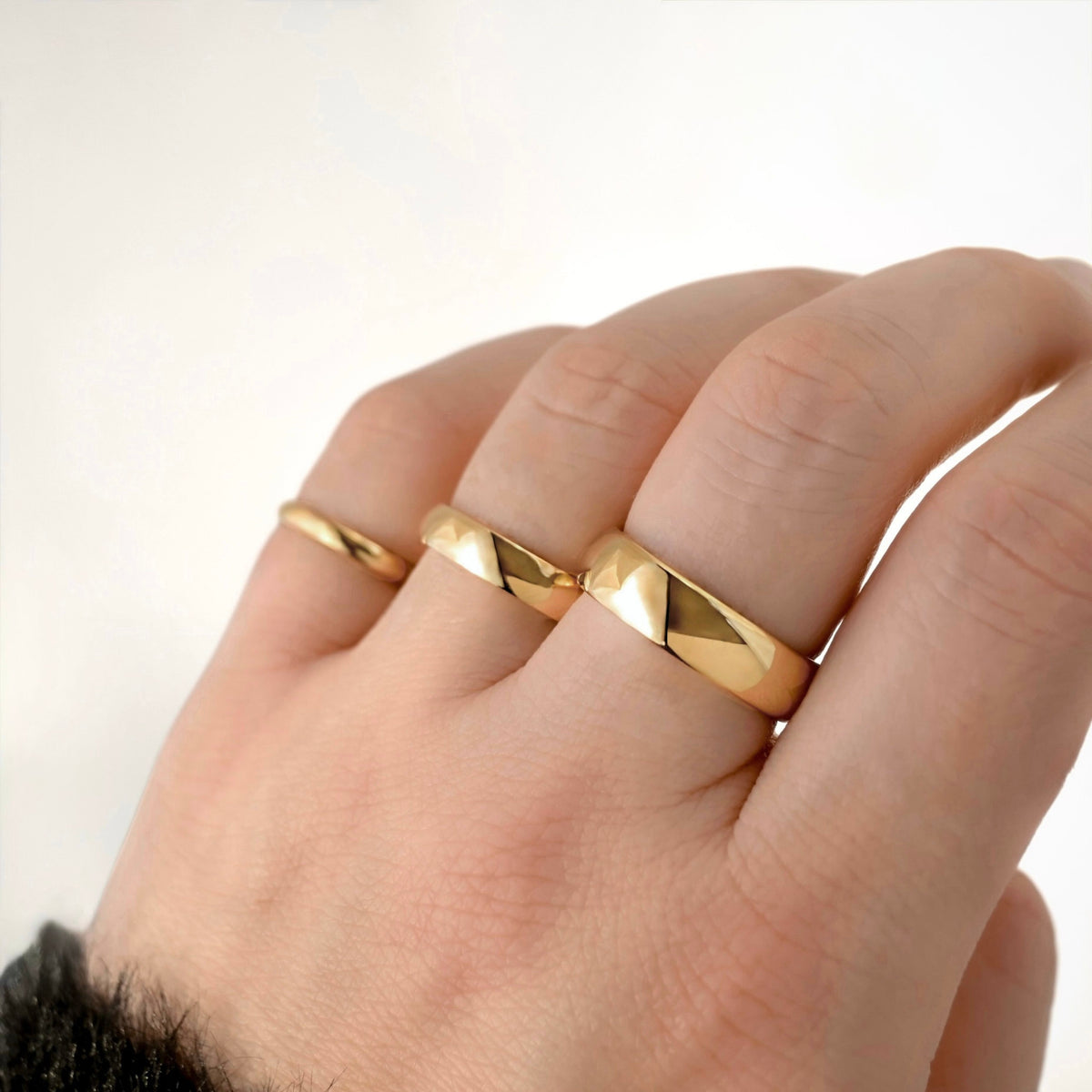 Hand wearing Three polished gold bands of different widths 