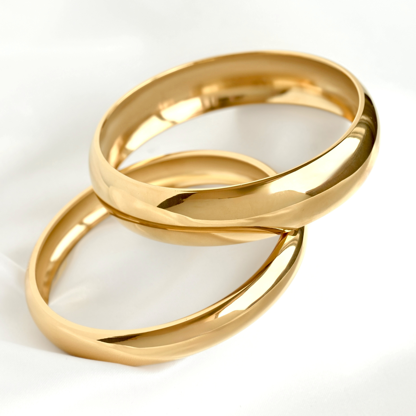 Two polished gold bangle bracelets interlocking on a clean white background.