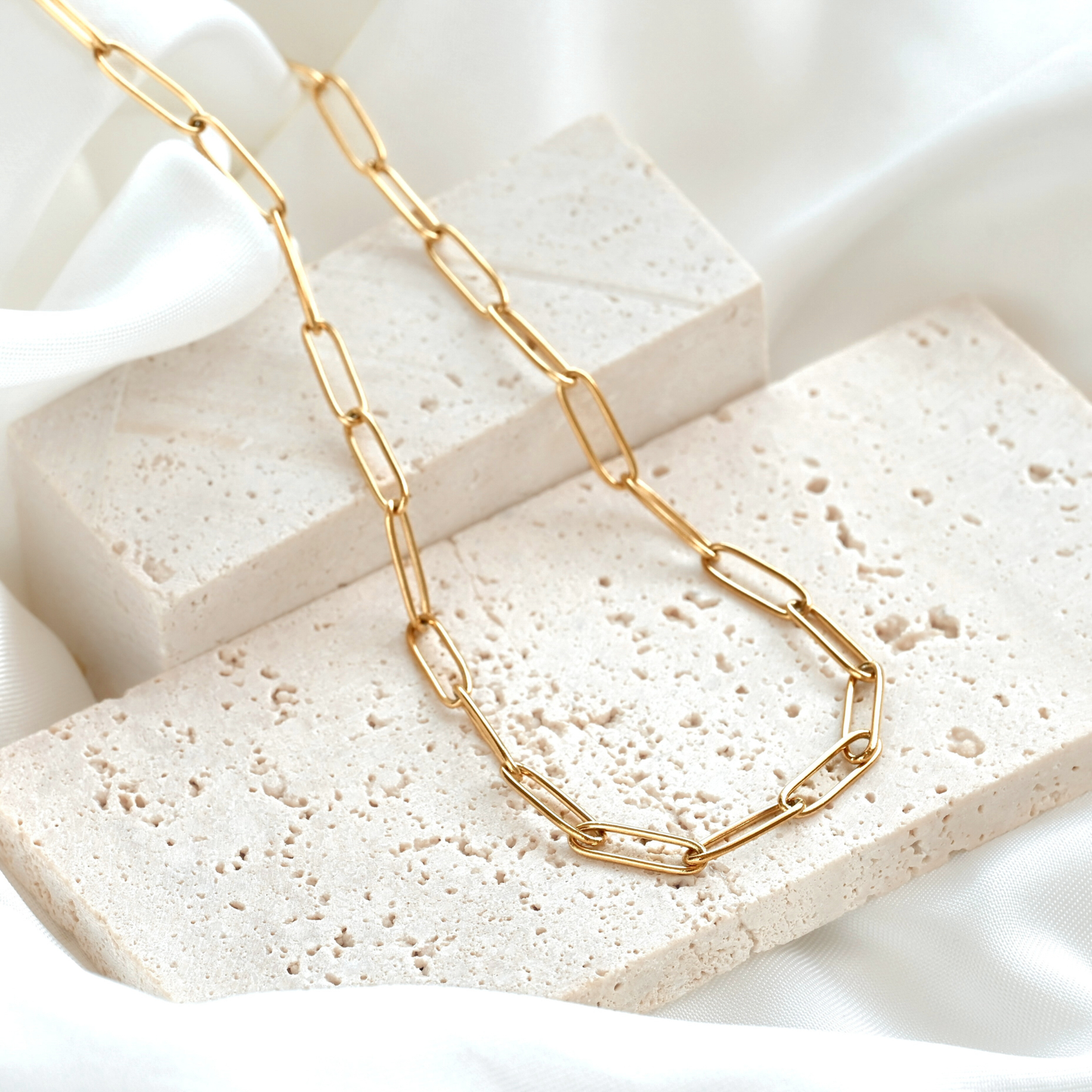 Gold chain necklace with elongated paperclip links  on a textured stone surface