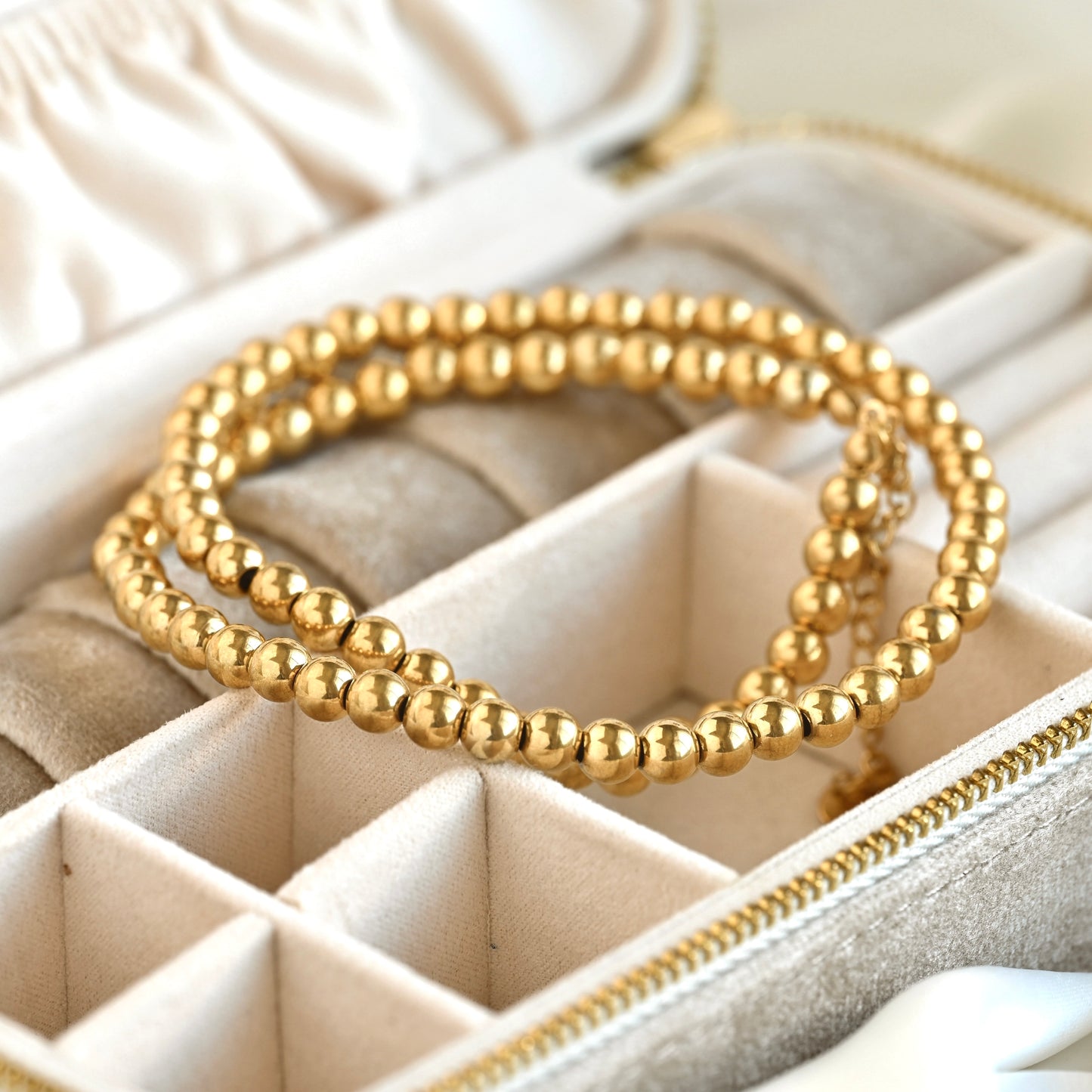 A gold beaded necklace resting inside a cream-colored jewelry organizer tray.