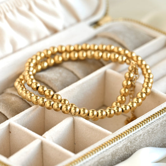 A gold beaded necklace resting inside a cream-colored jewelry organizer tray.