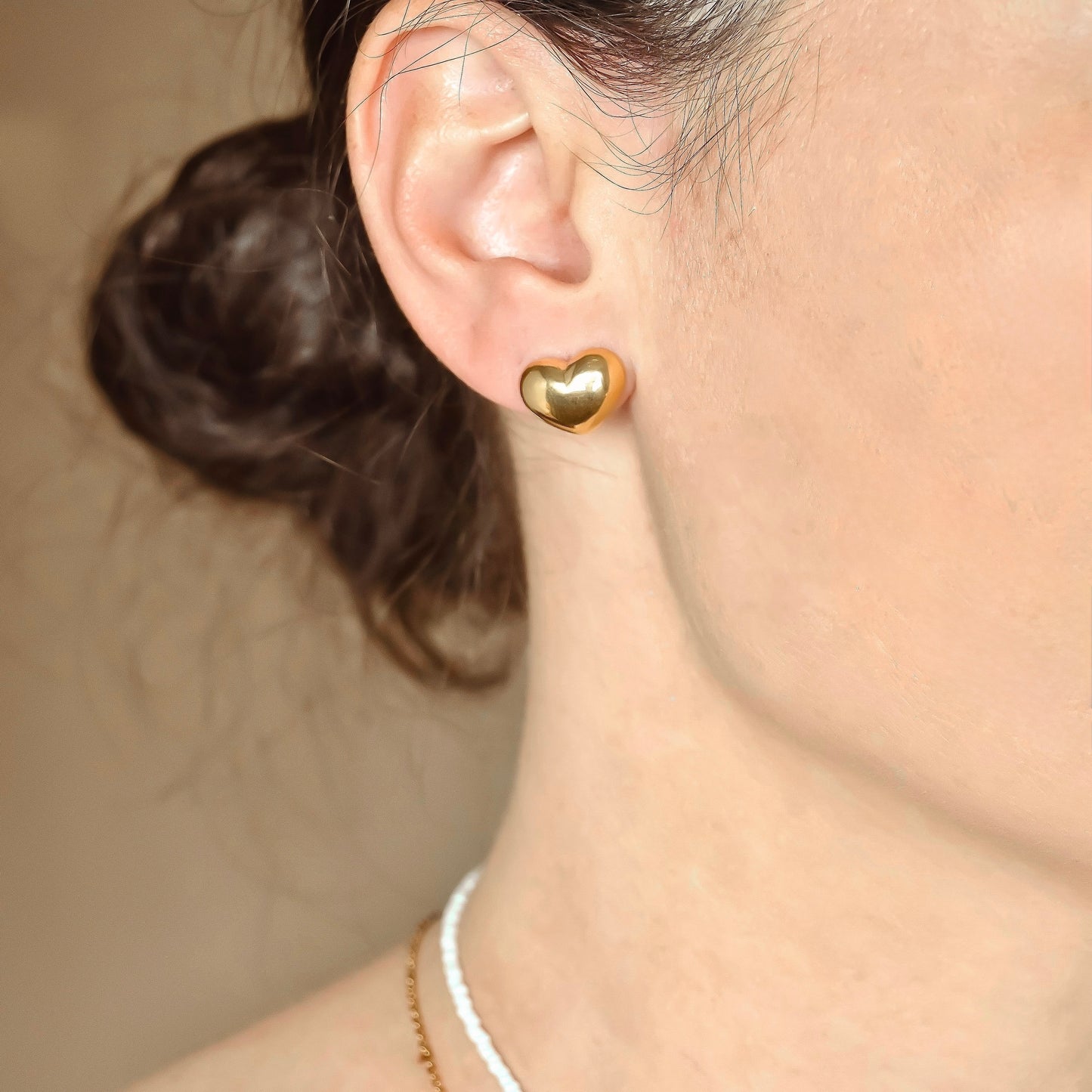 Gold heart earring worn by a person with a neutral background