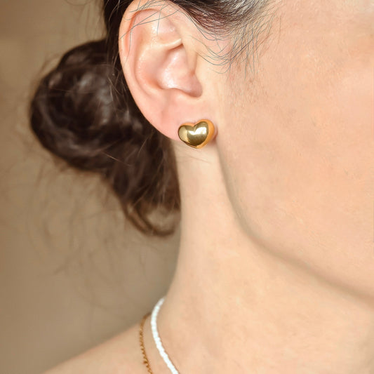 Gold heart earring worn by a person with a neutral background