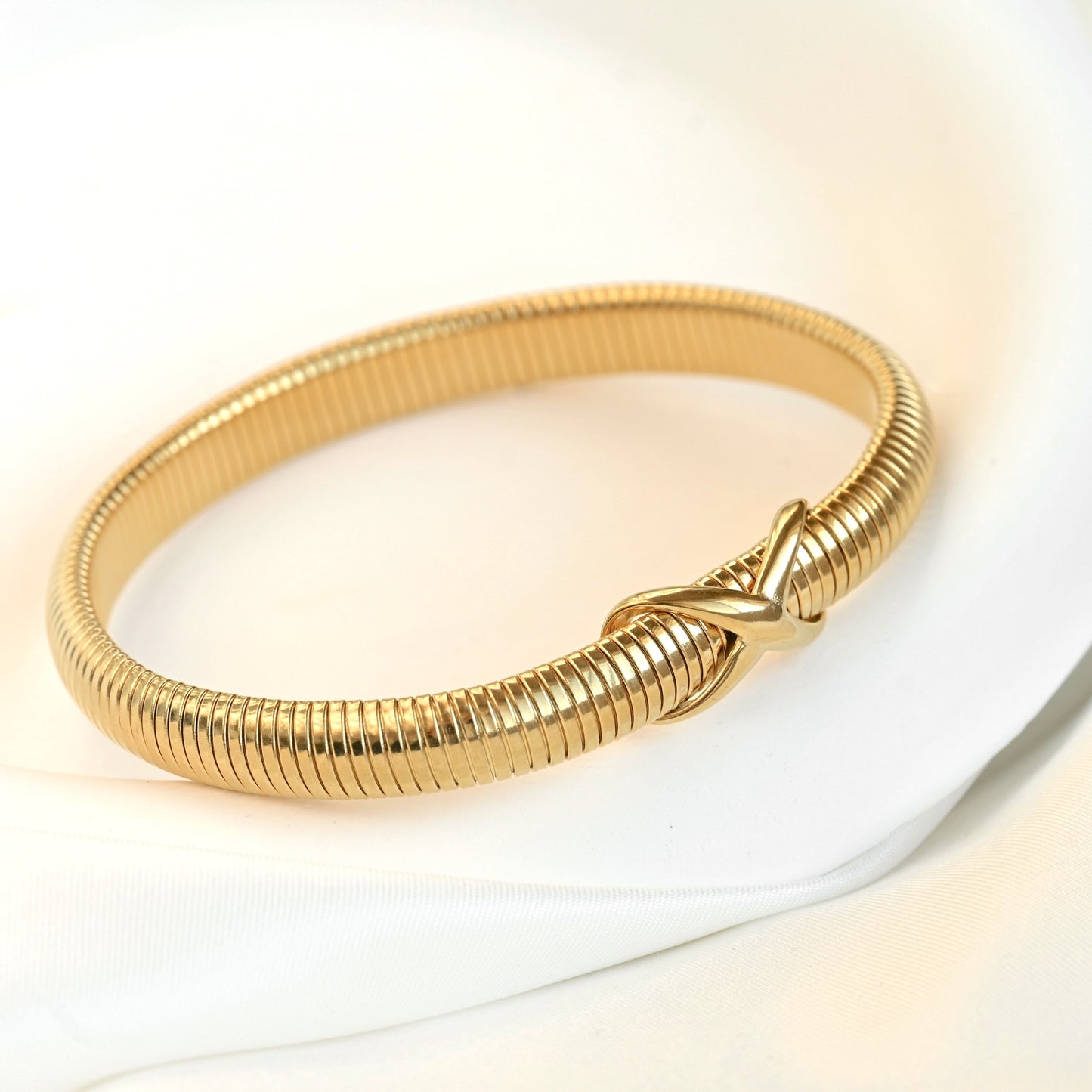 Thin gold  tubogas bangle with an infinity know in the front on a white background