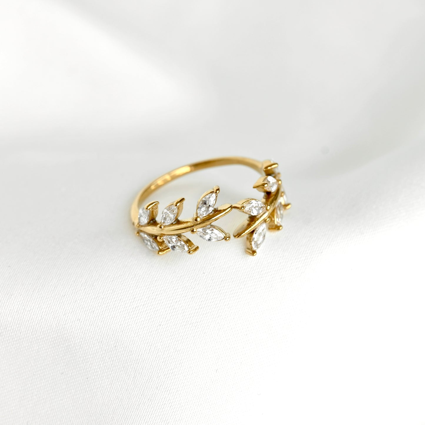 A gold leaf and vine ring adorned with marquise-cut clear crystals, resting on a soft white fabric background.