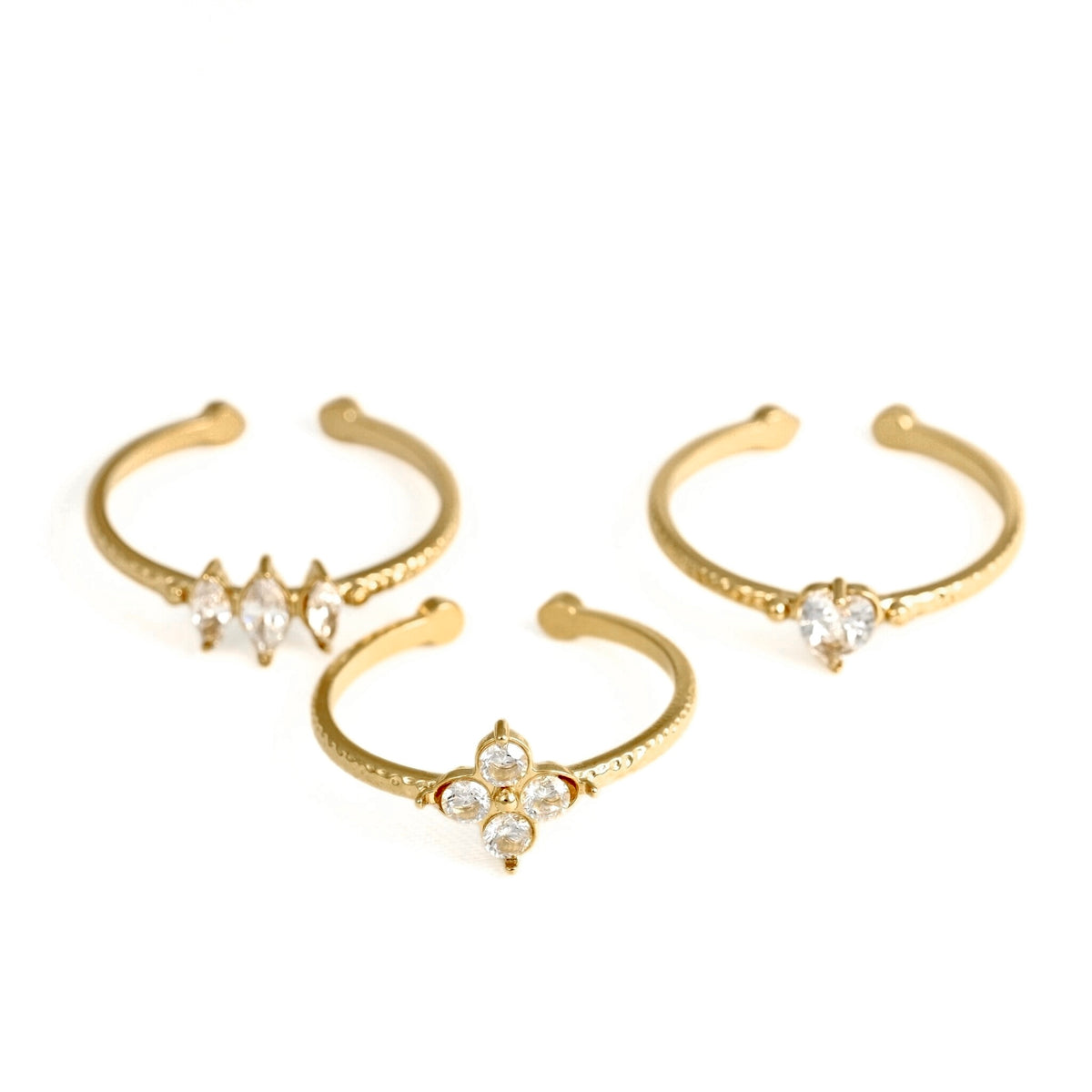Three gold-toned open bangle rings with clear rhinestone floral and geometric center details, arranged on a plain white background.