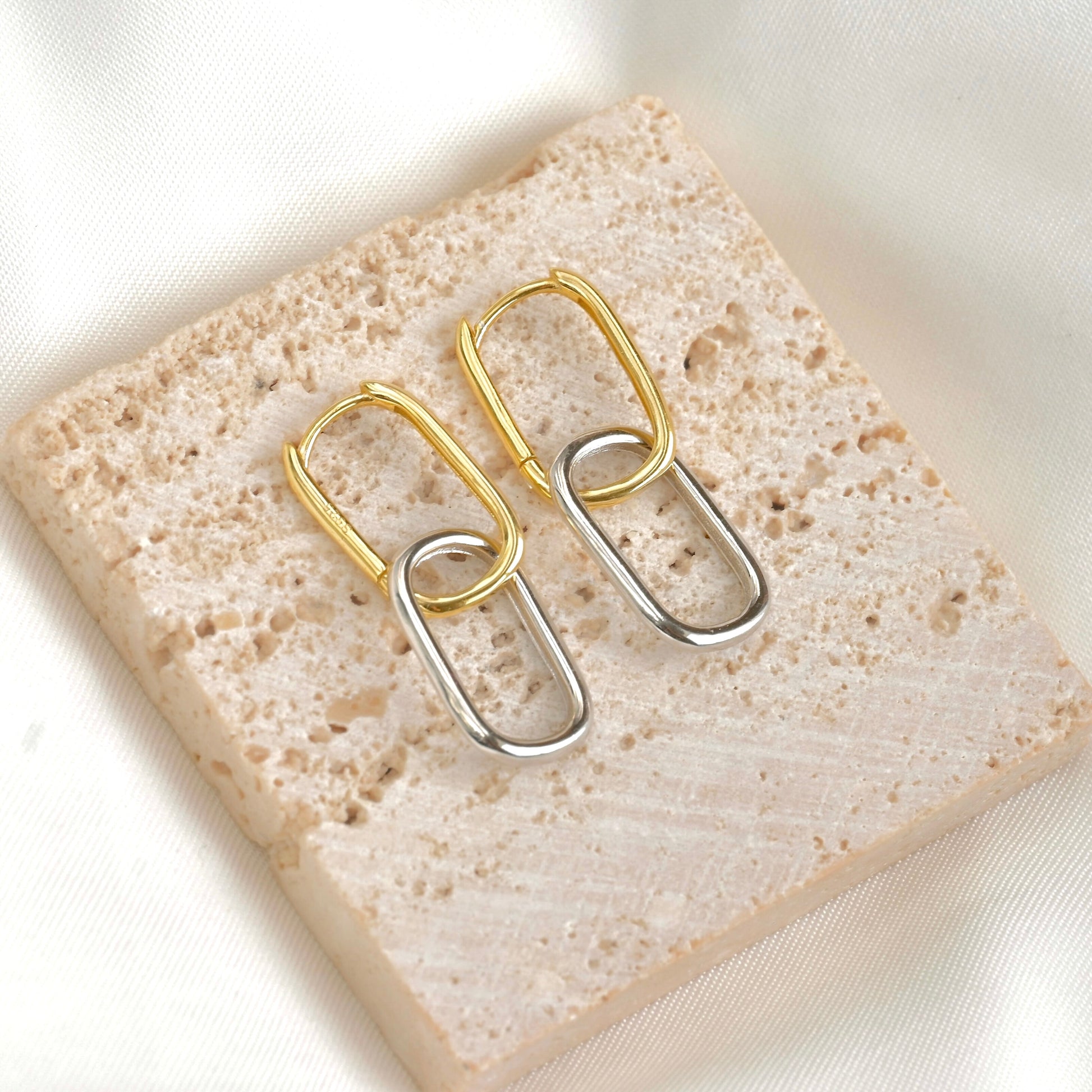 Pair of rectangular two tone earrings with top link gold and bottom link silver on a textured stone surface