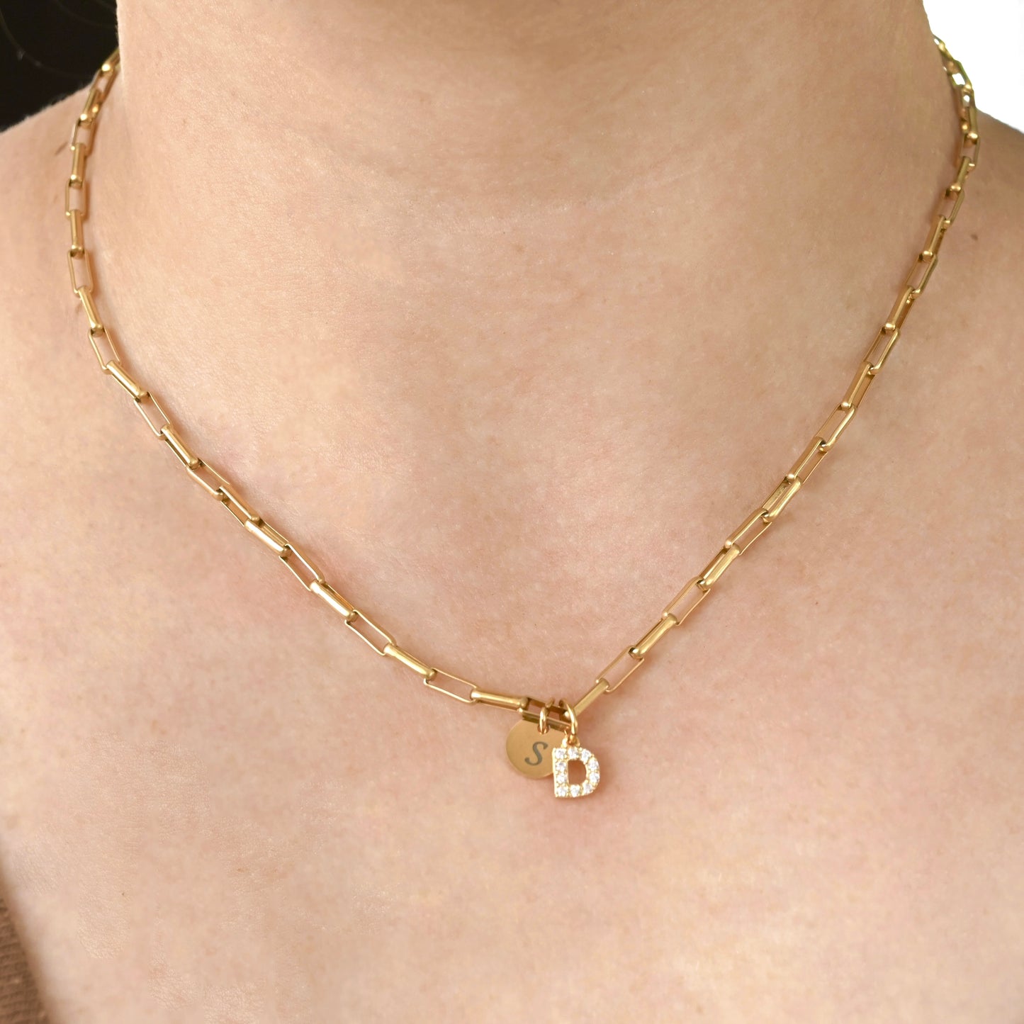 Gold bold paperclip necklace with a small round letter disc and pave CZ 'D' pendant on a person's neck