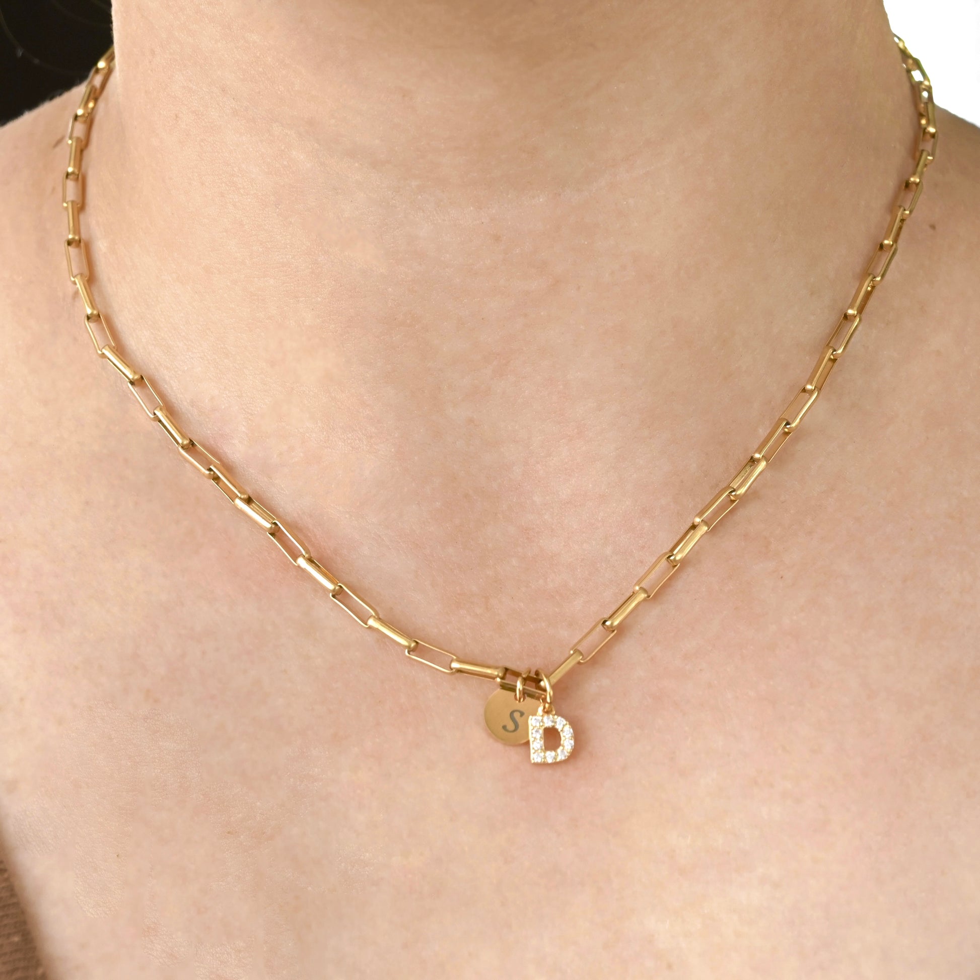 Gold bold paperclip necklace with a small round letter disc and pave CZ 'D' pendant on a person's neck