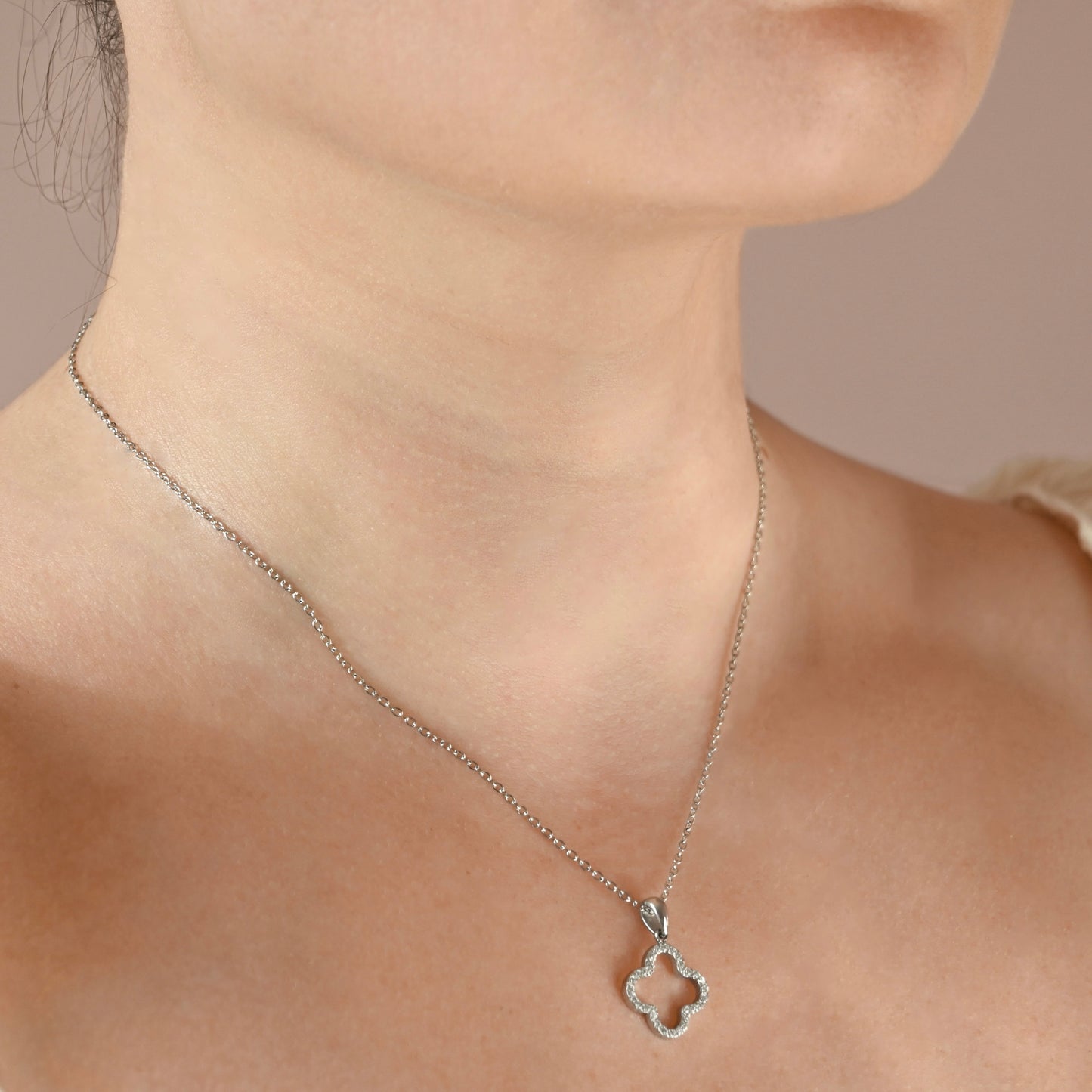 A silver necklace with a clover pendant adorned with small clear crystals on a person's neck.