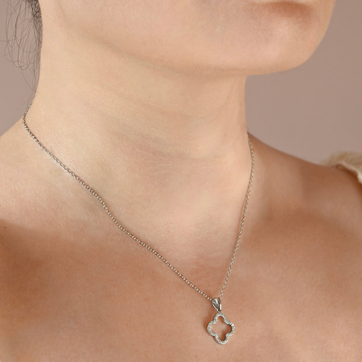 A silver necklace with a clover pendant adorned with small clear crystals on a person's neck.